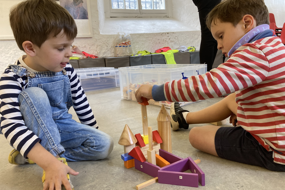 Two early years children are sitting on the floor using coloured wooden blocks to build a castle.