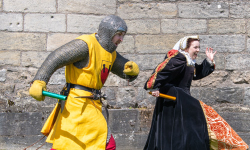 Two people dressed in period costume smiling and running doing a relay race