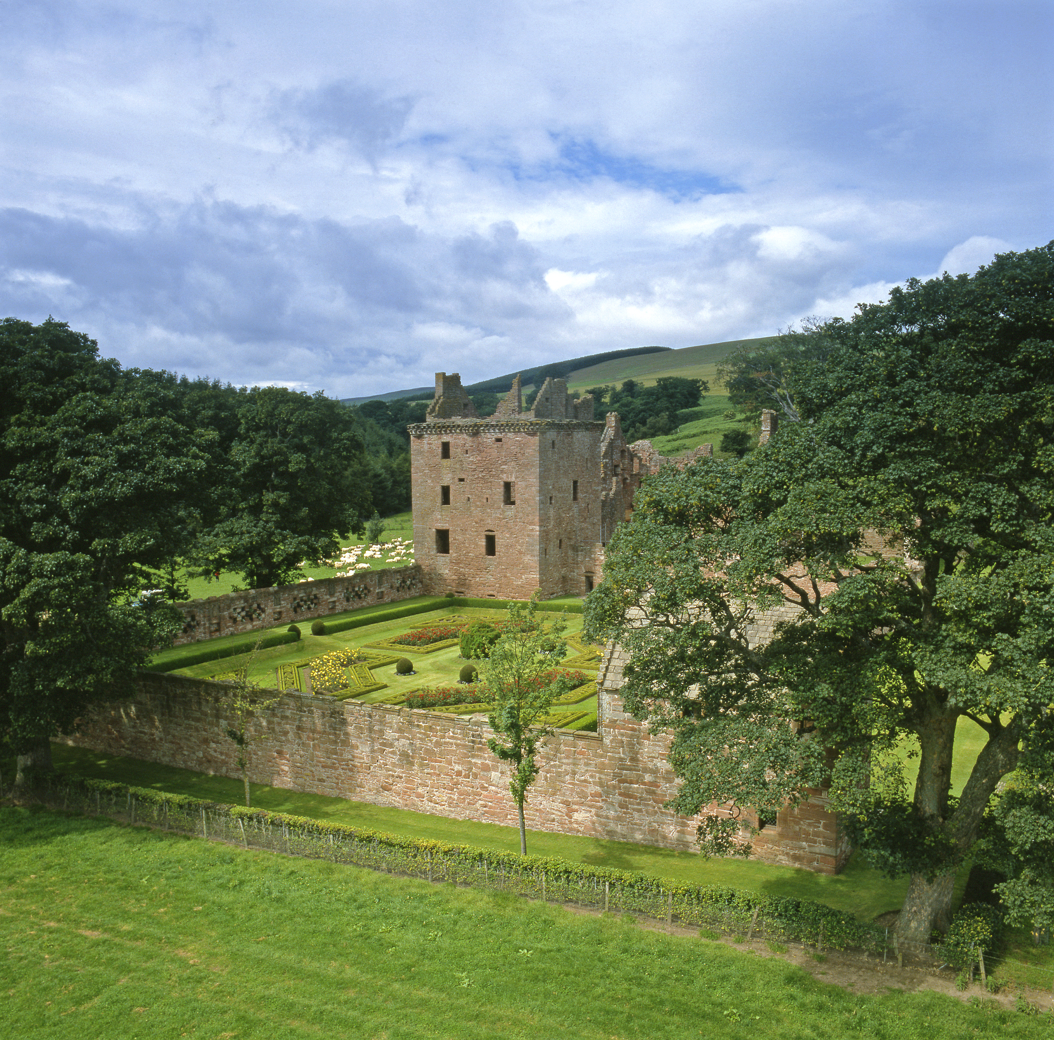 Lush green trees and fields surrounding a ruined castle and a neat walled garden