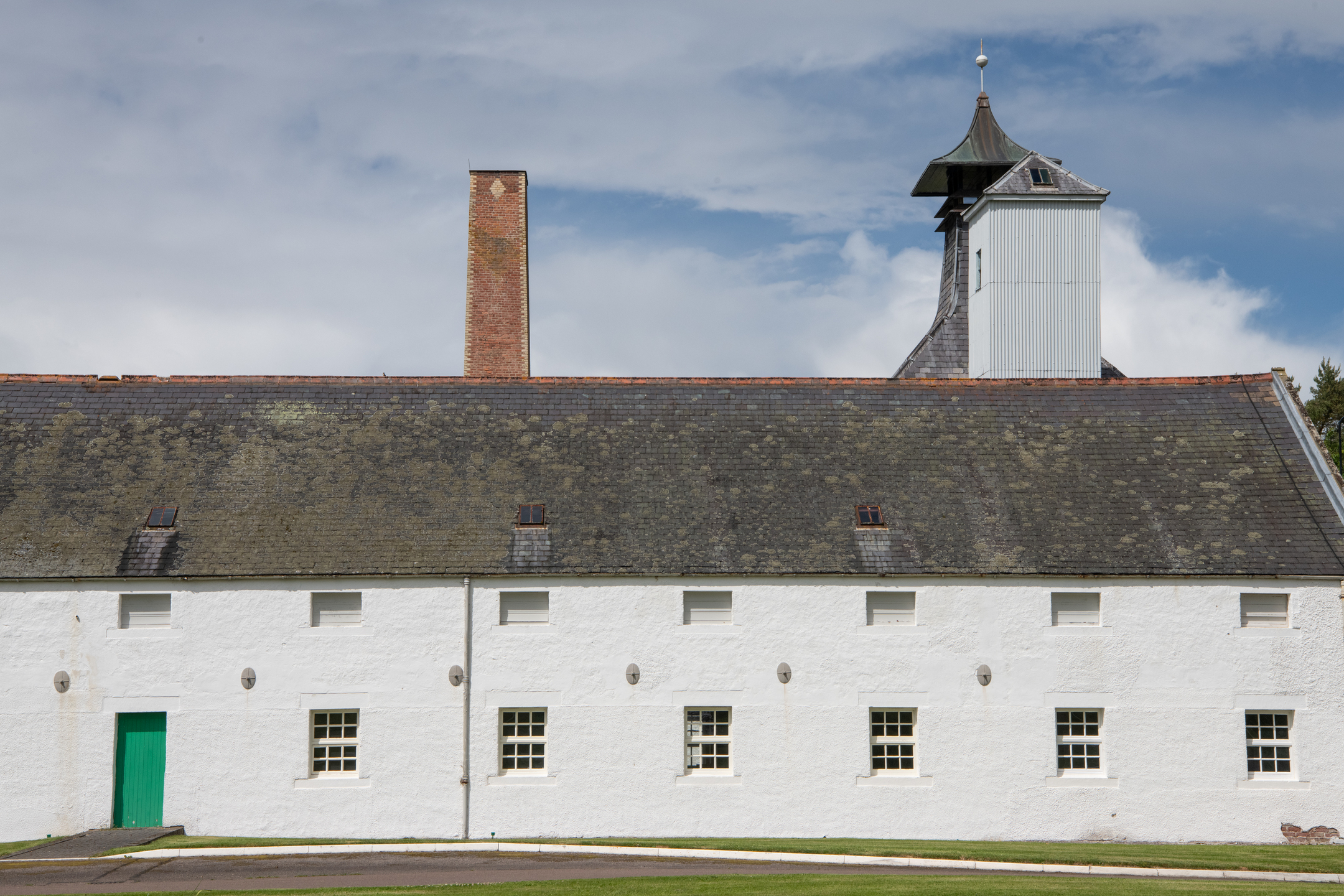 Whitewashed warehouse building at Dallas Dhu distillery, with a tall brick chimney and traditional pagoda-style roof ventilation.