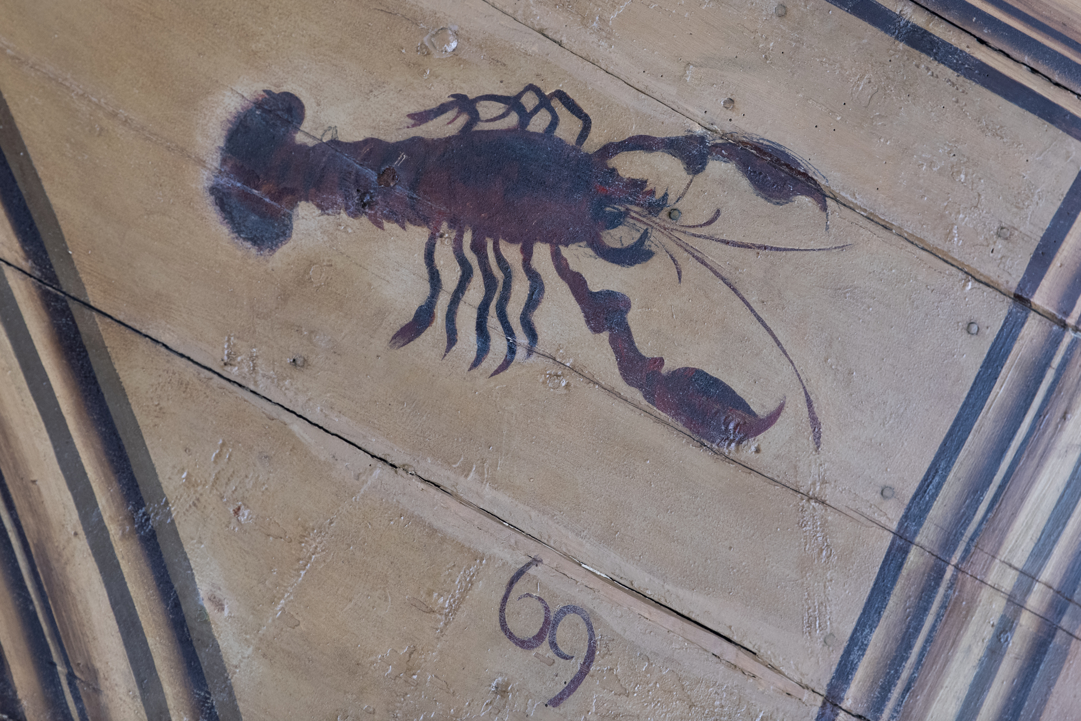 Painted depiction of a dark red and black lobster-like creature on wooden ceiling panels, accompanied by the number 69 beneath the artwork.