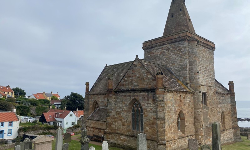 A church with gravestones in a cemetery and houses and sea surrounding