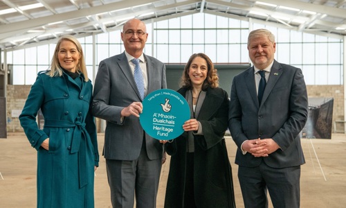 Four people smiling at the camera holding a sign of the logo of the heritage fund. 
