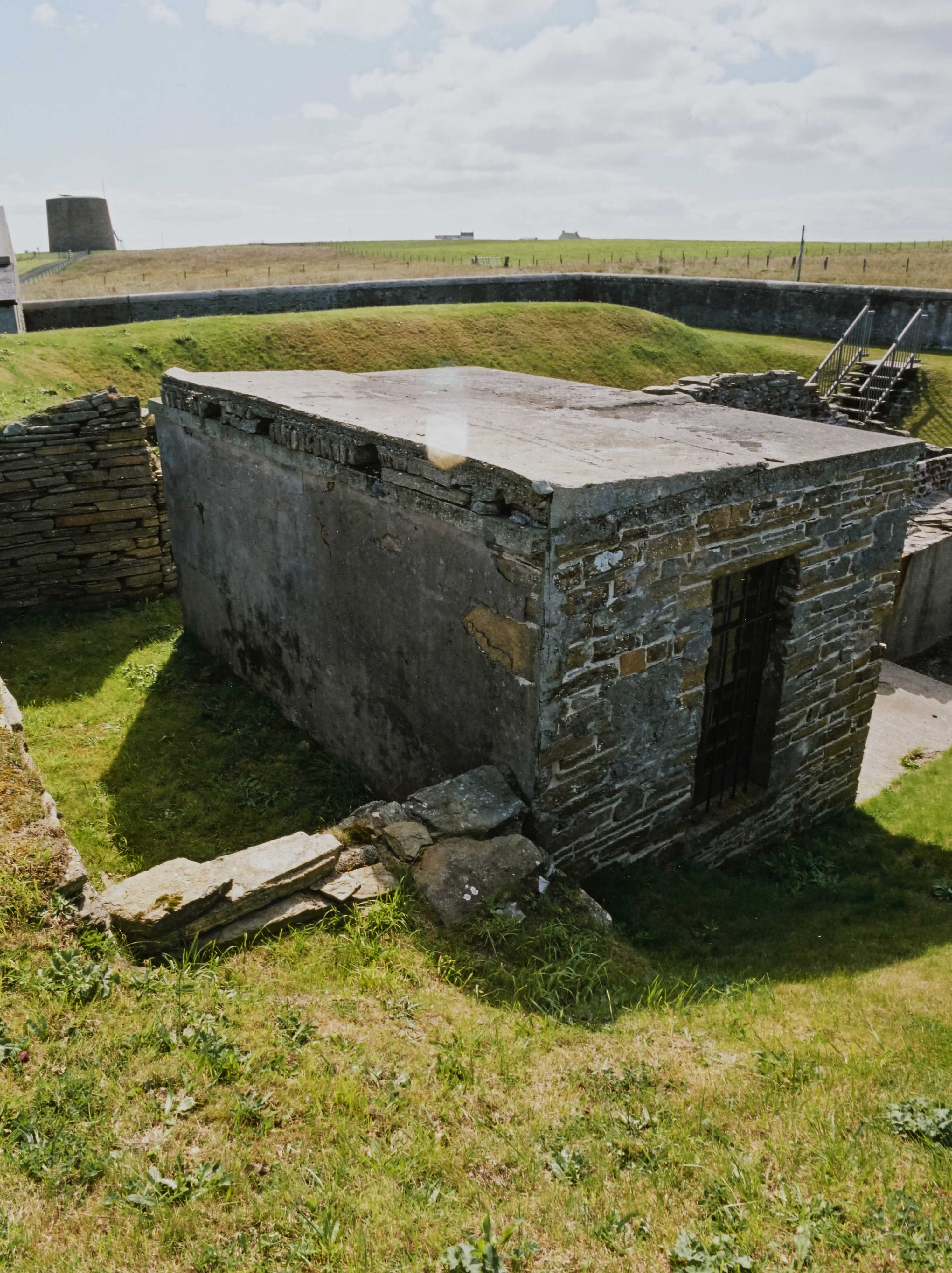 A small stone building with a narrow door way, surrounded by a perimeter wall 