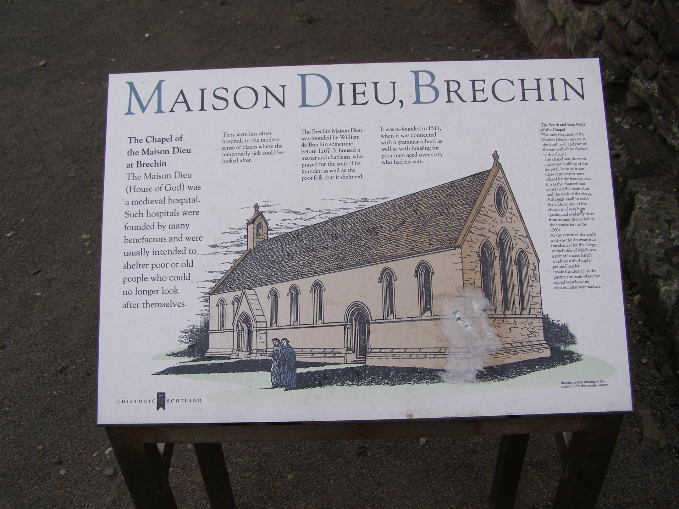 Interpretive sign titled ‘Maison Dieu, Brechin’ featuring historical text about the medieval hospital and an illustration of the chapel as it originally appeared, with a pitched roof, bellcote, and multiple arched windows. The panel explains the building’s function as a charitable hospital for the poor and elderly