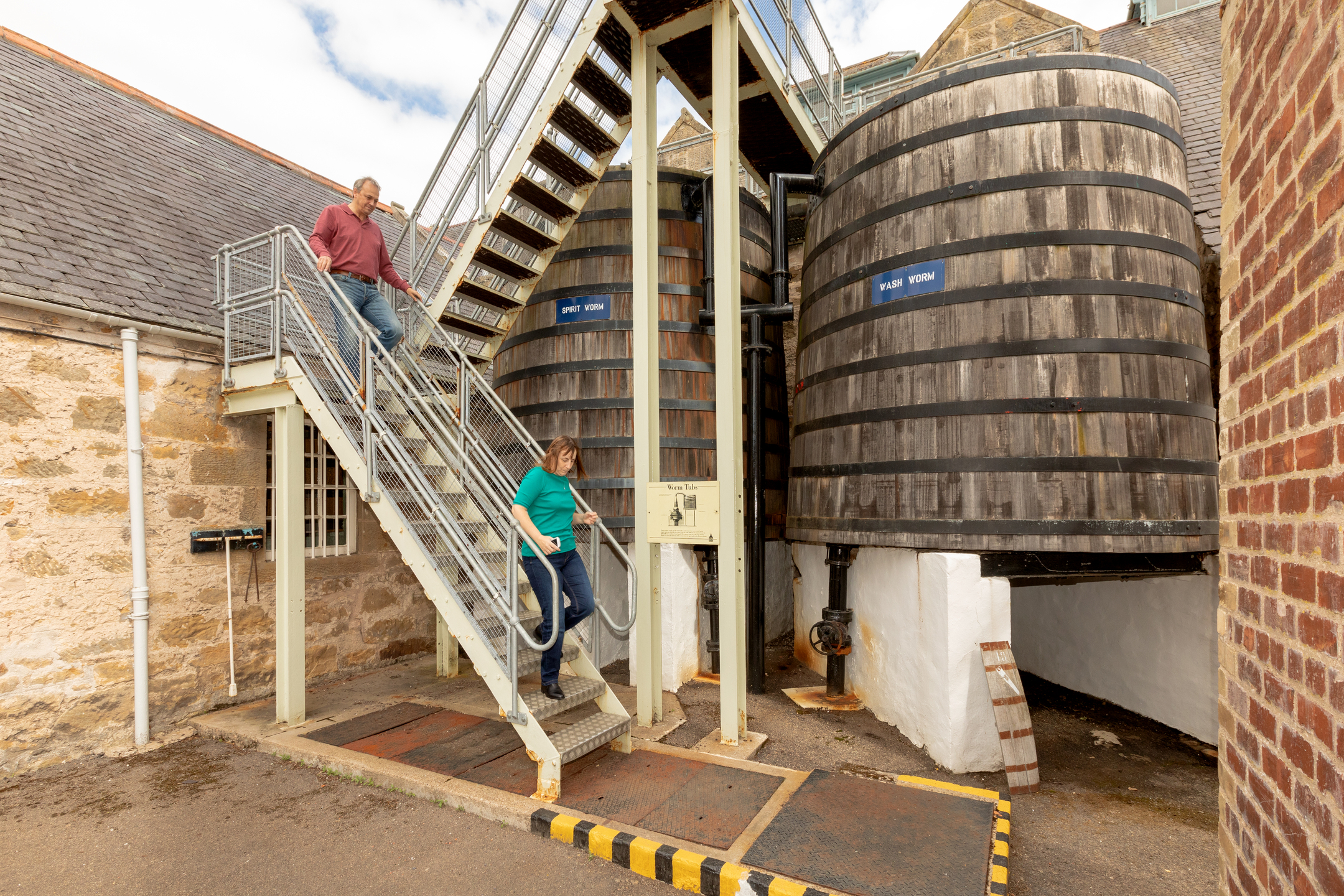 Visitors descend a metal staircase beside large wooden worm tubs.