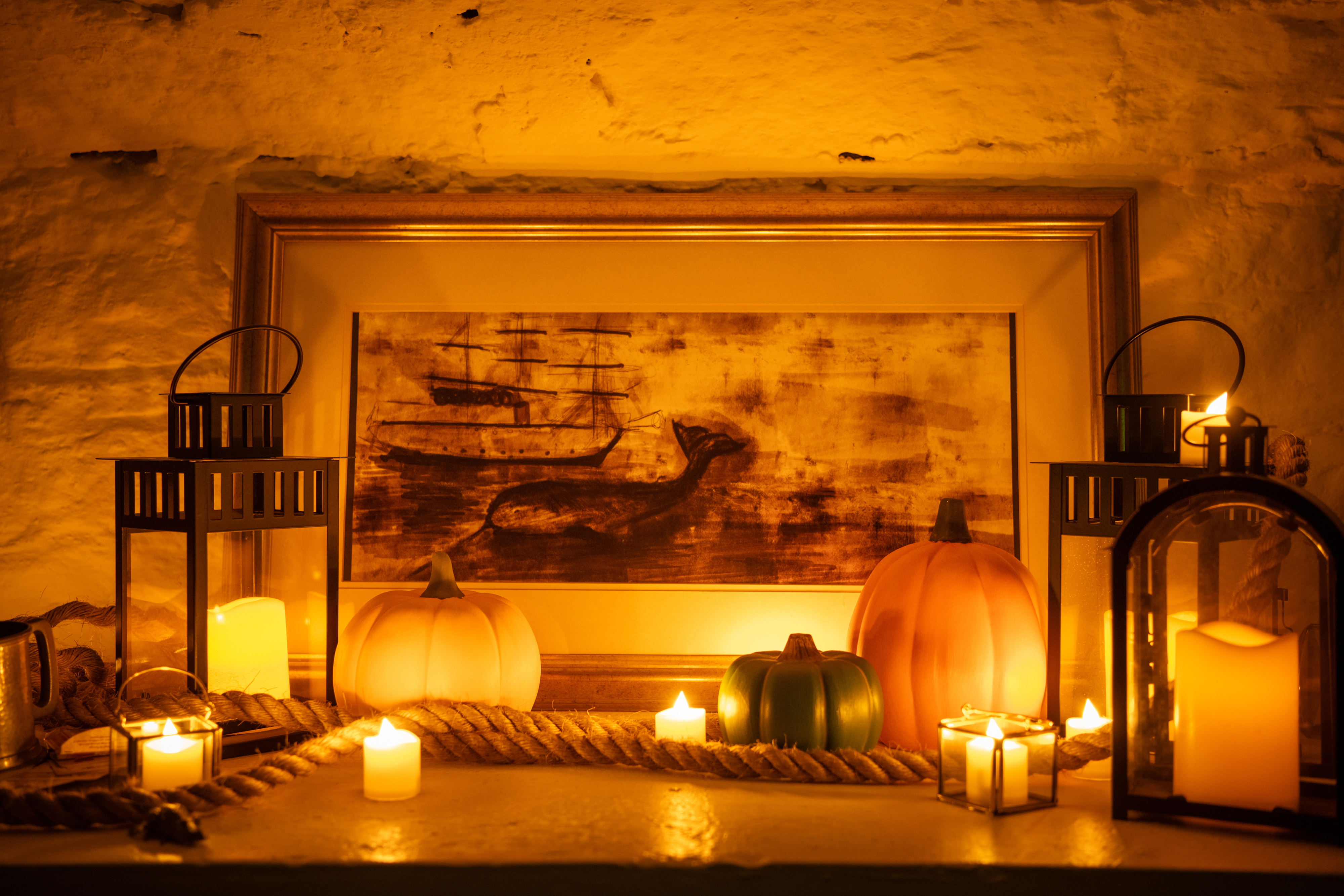 Painting of a ship next to lit candles and pumpkins with atmospheric lighting. 