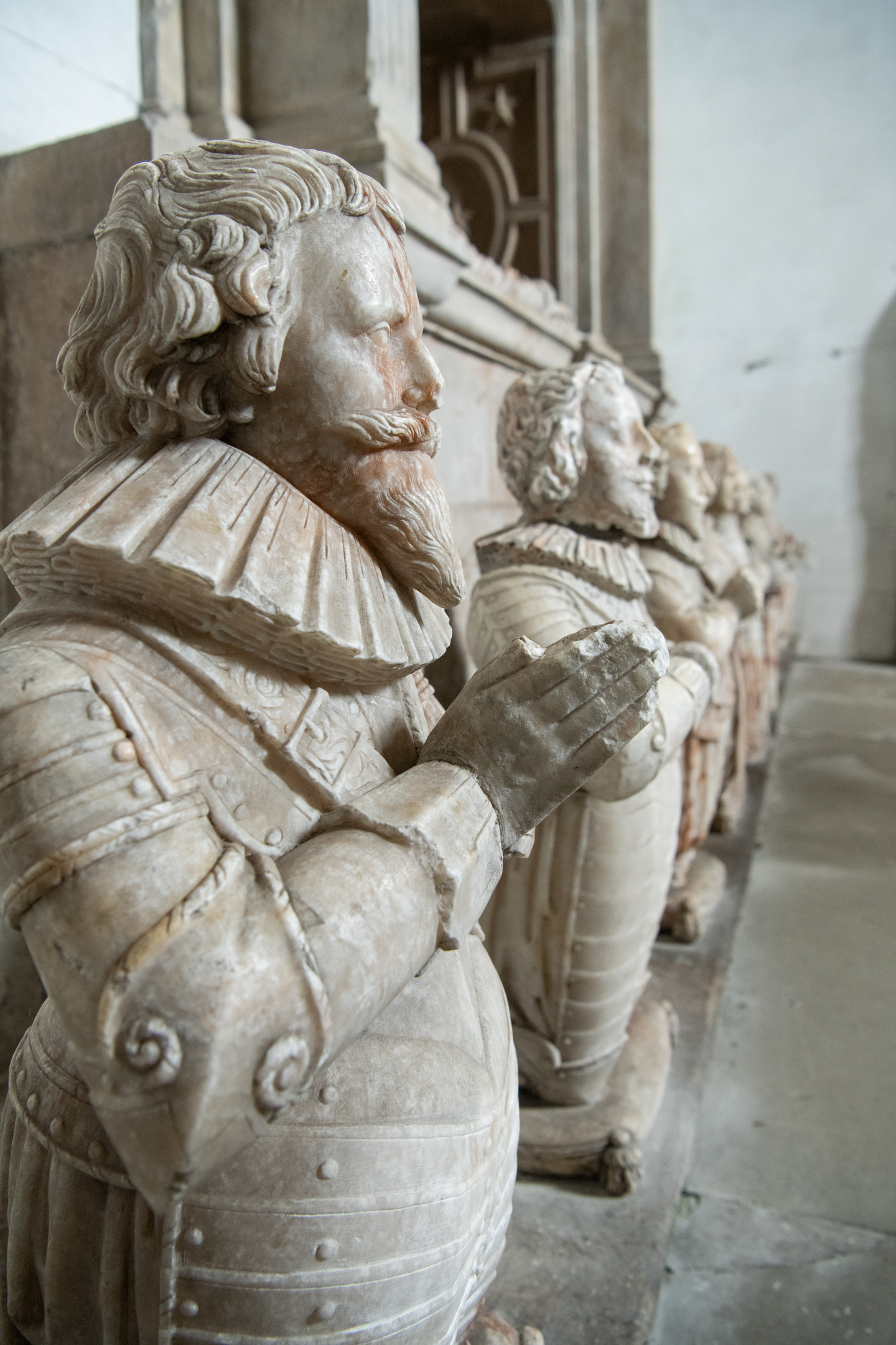 A close-up view of stone effigies inside Culross Abbey, showing detailed carving of ruffled collars, folded hands, and period clothing, arranged in a row along a tomb.