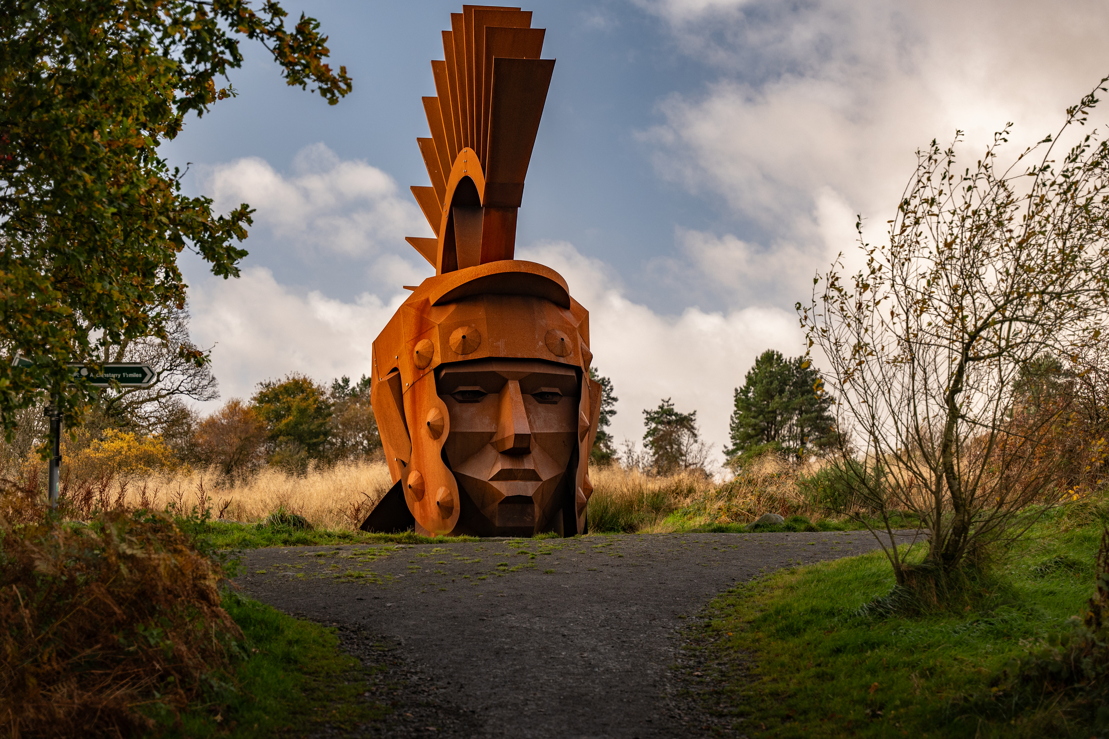 Large roman head sculpture beside a path surrounded by grass and trees