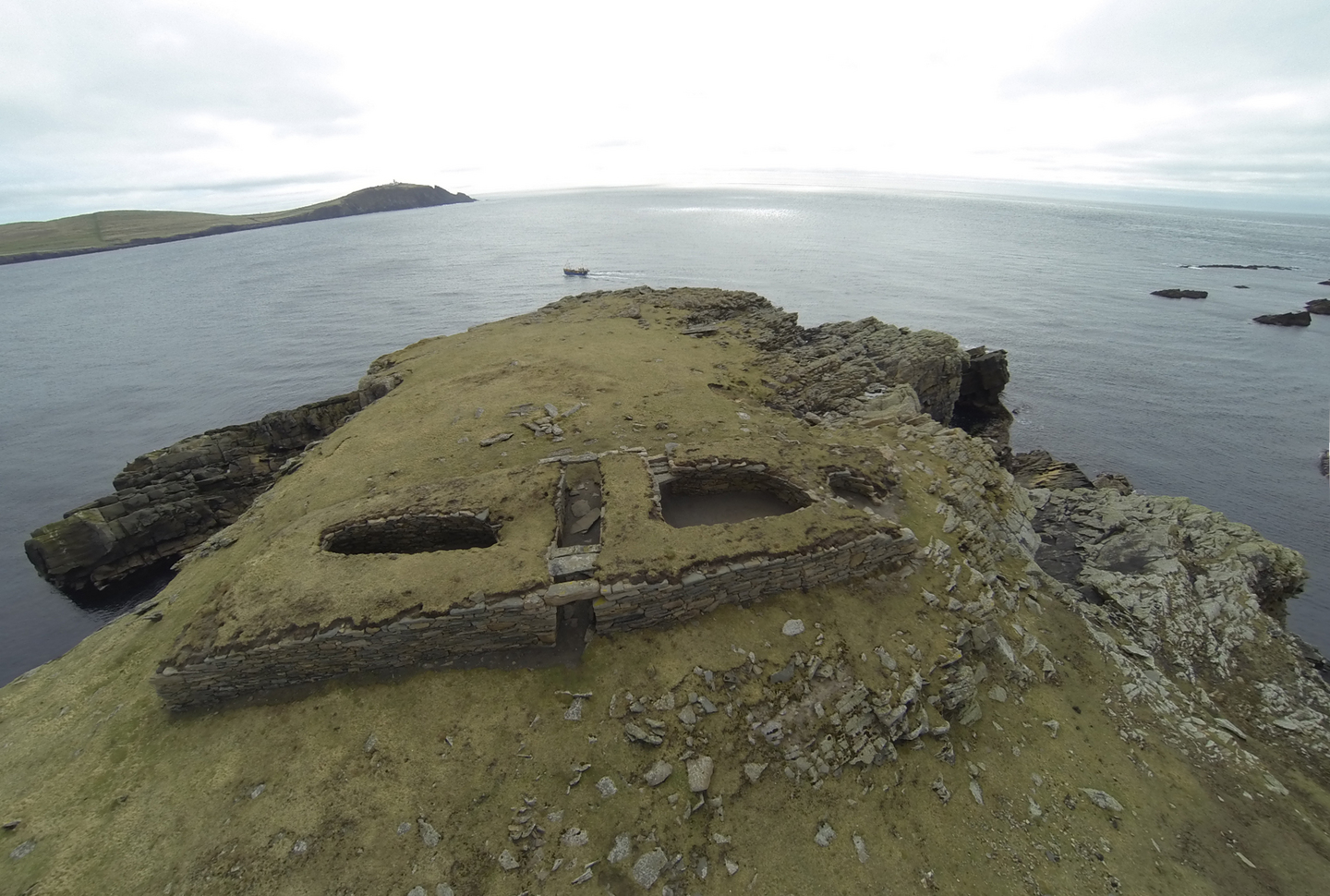 A stone built structure, you can see the edge of the cliff either side and the sea surrounding.