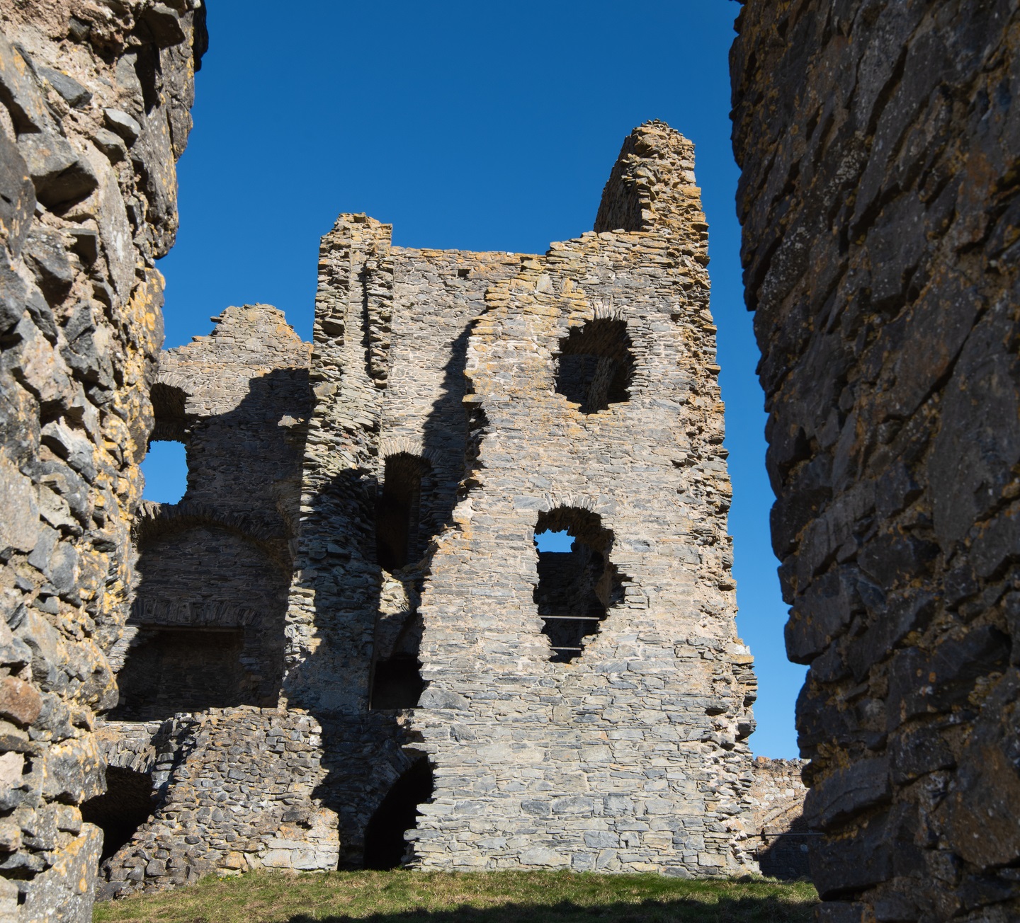 Close-up of the ruins of a stone castle. A tower has jagged holes in its walls. 