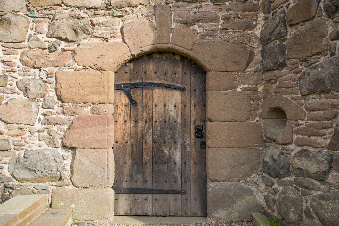 A door with wood panels, in the middle of a stone wall. 