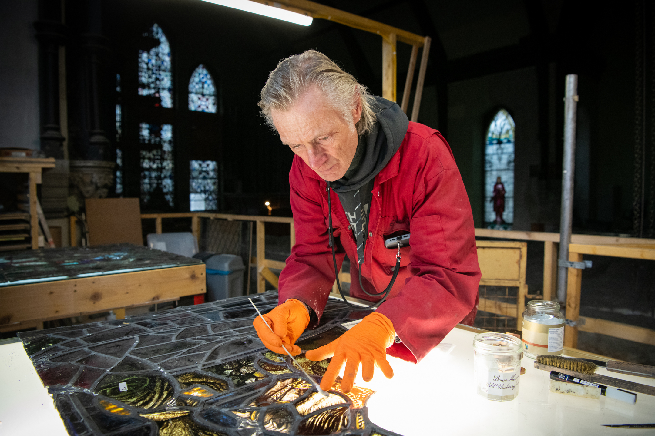 Man gently cleaning parts of a stained glass window which is laying on a light box table.
