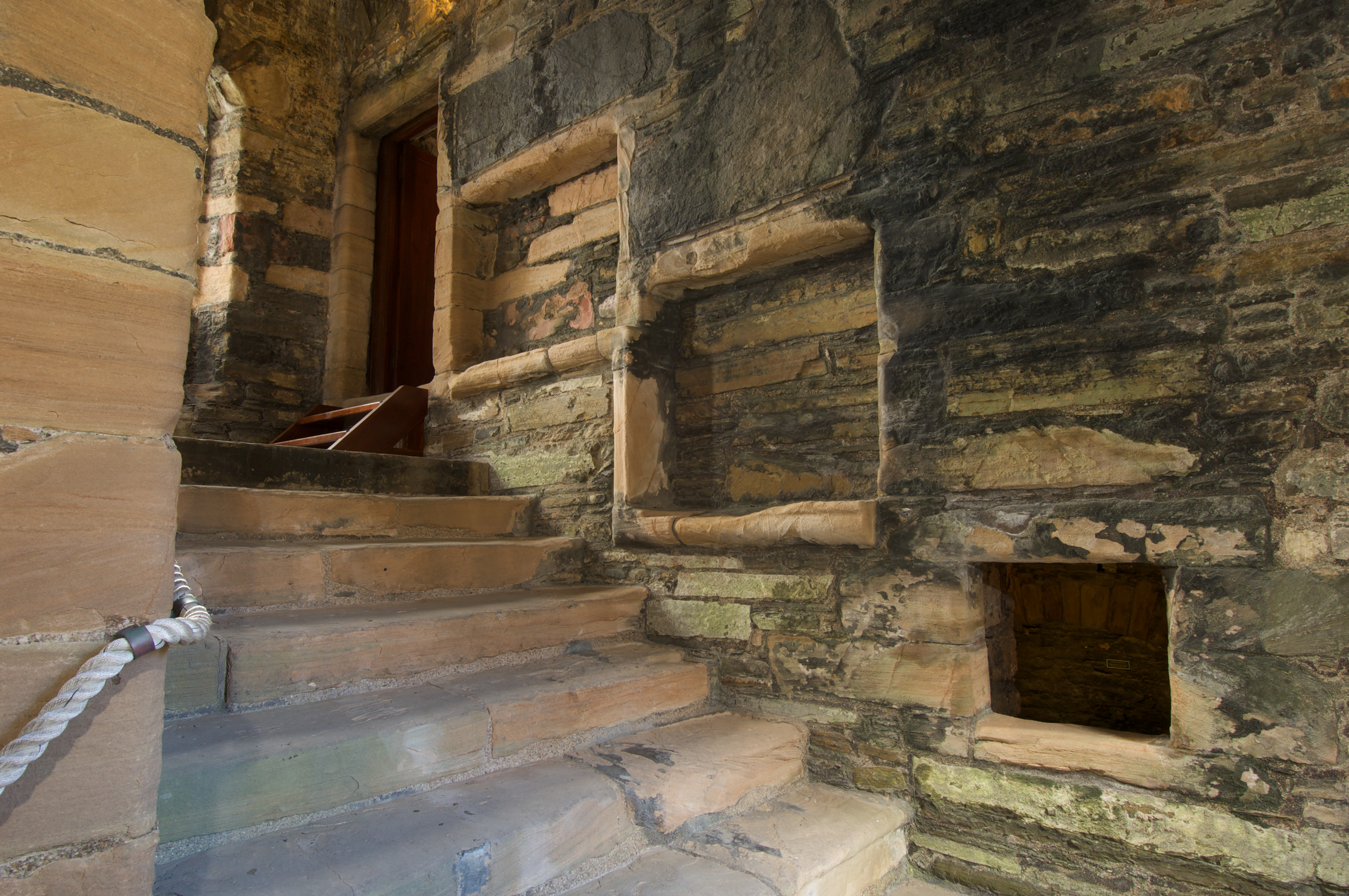 Stone steps leading to a doorway inside a palace ruin, surrounded by textured stone walls and alcoves.