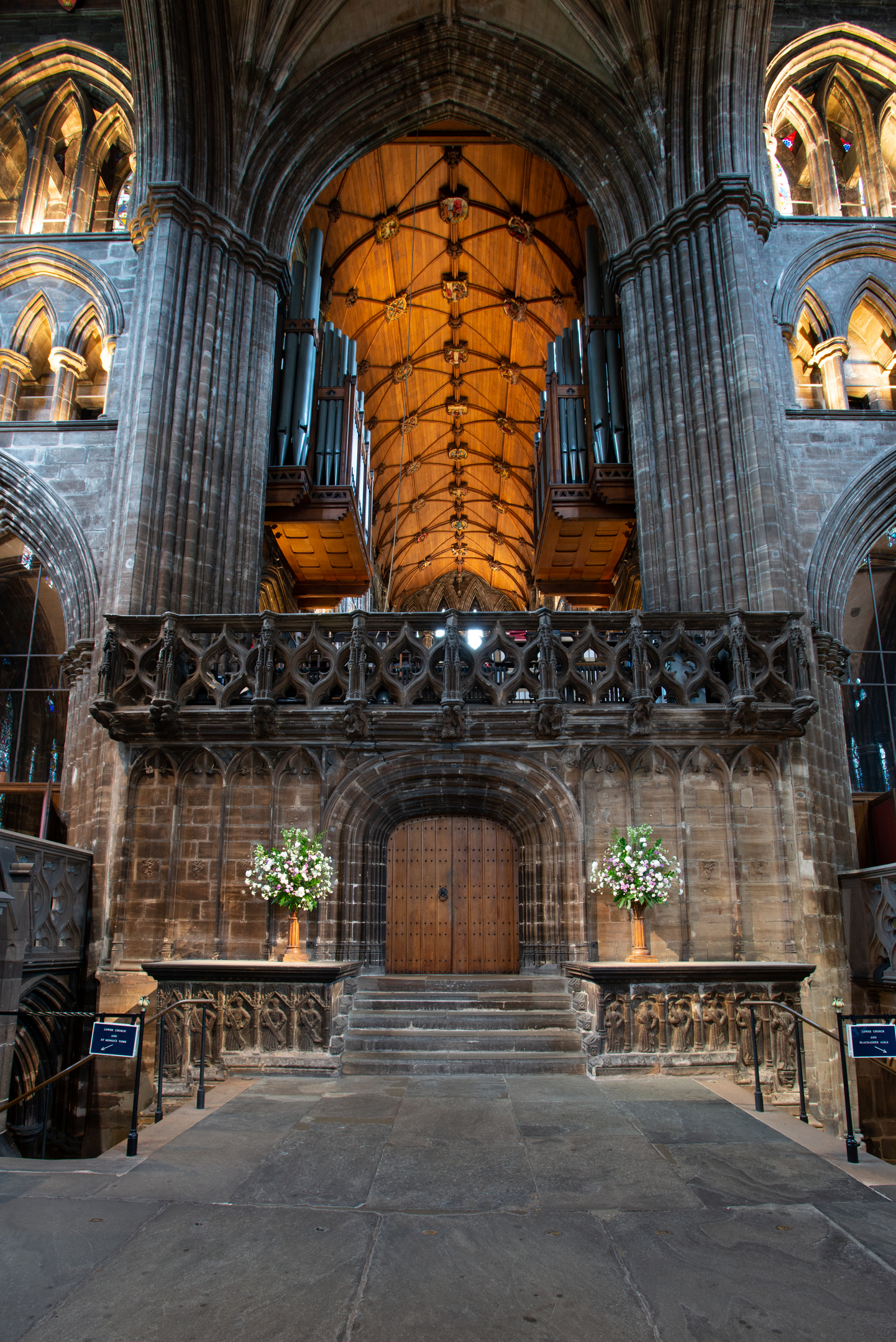 Grand interior view facing the cathedral’s central crossing, showing a high arched doorway, ornate stone balcony, wooden ceiling and large organ pipes.