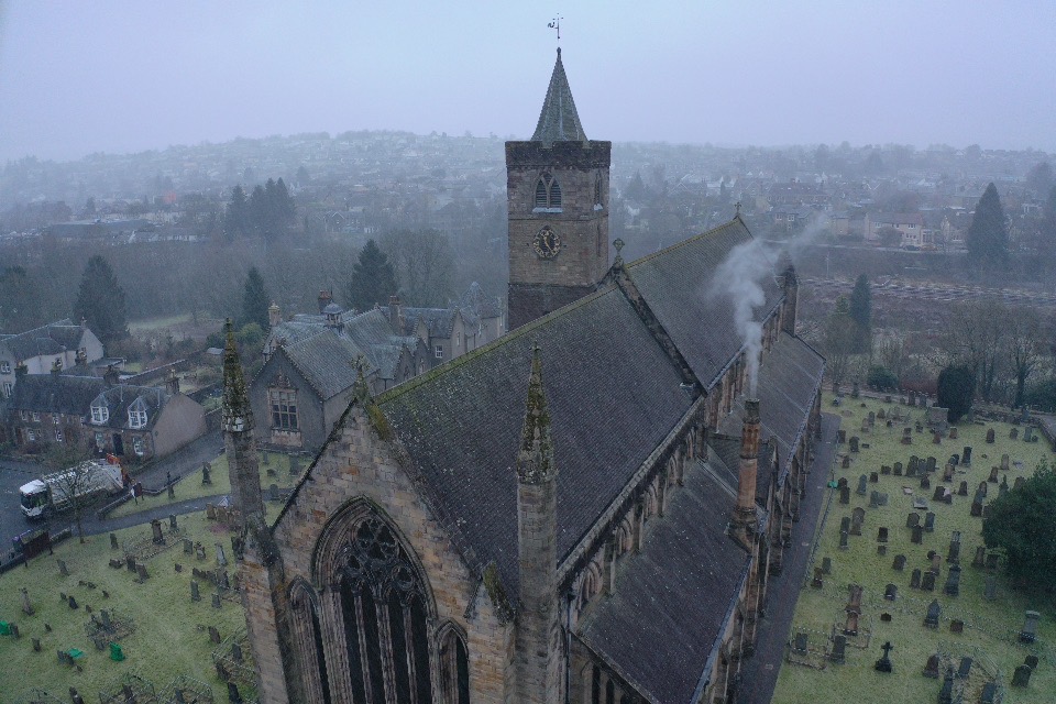 Drone image of a cathedral, and its surrounding graveyard and town, on a gloomy foggy day.