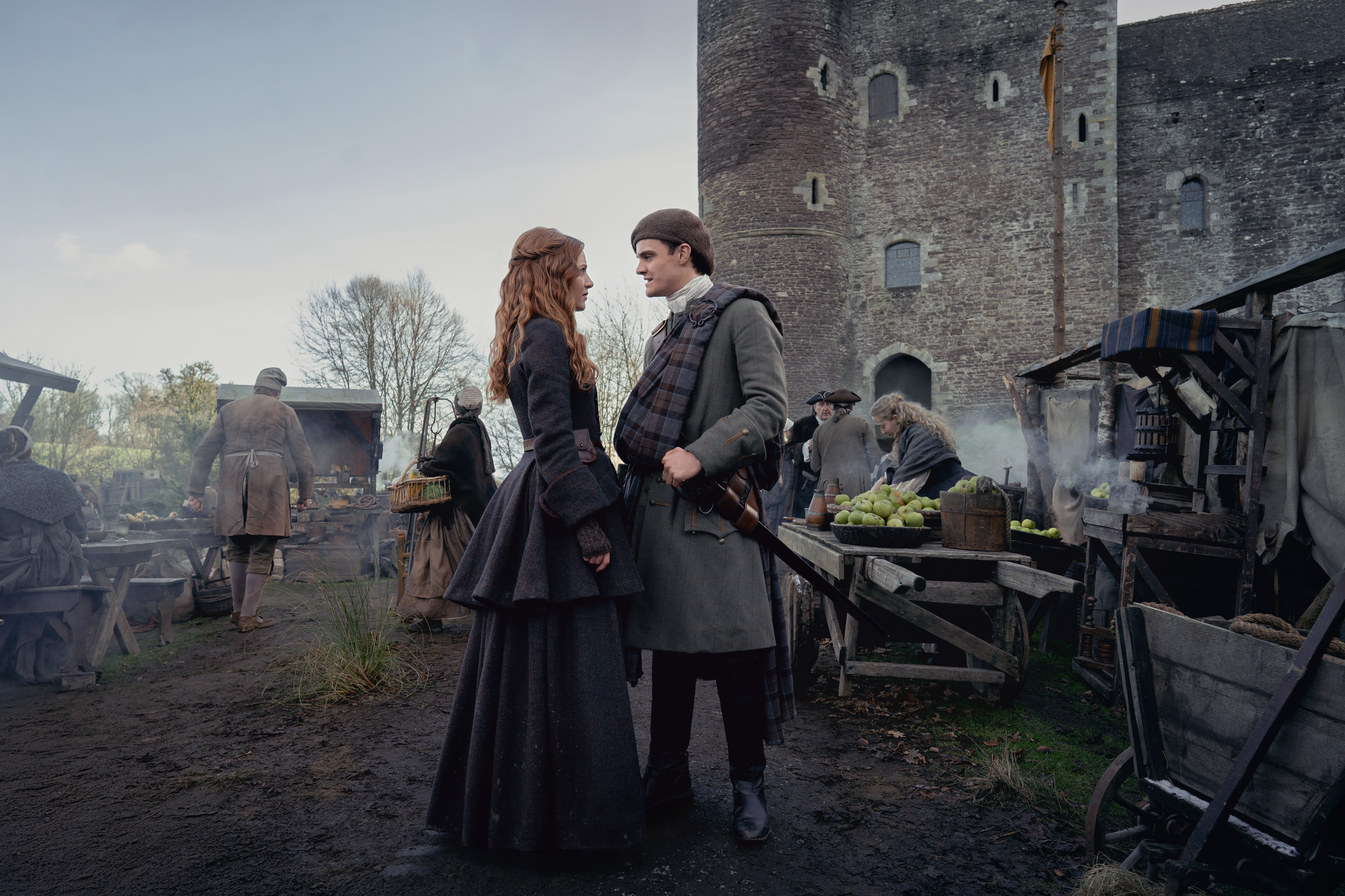 A shot form a TV show of a couple in period costume deep in conversation with the bustle activity of a medieval castle depicted in the background.