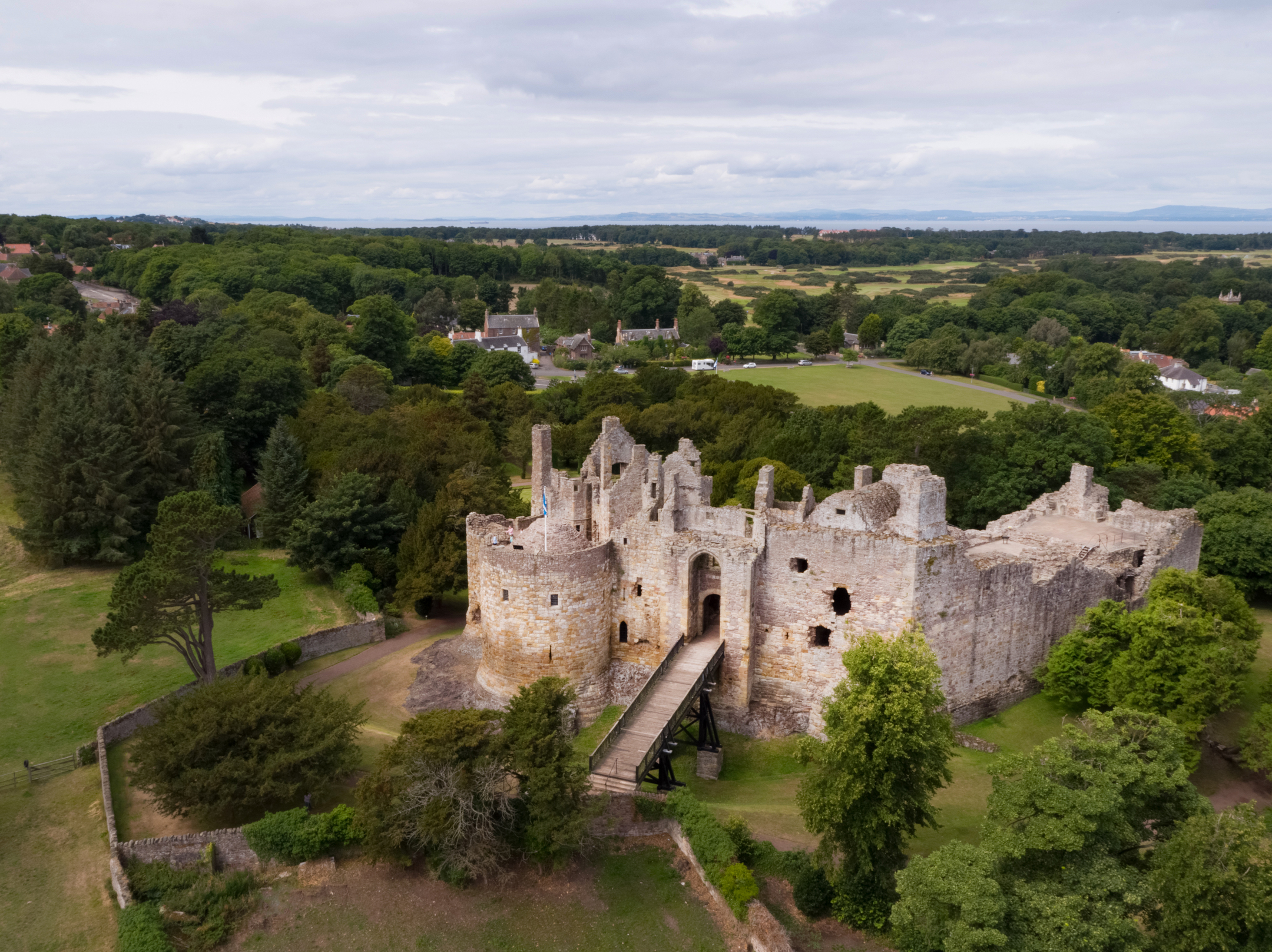 A castle with a wooden walkway up to the entrance, from an aerial viewpoint with trees around