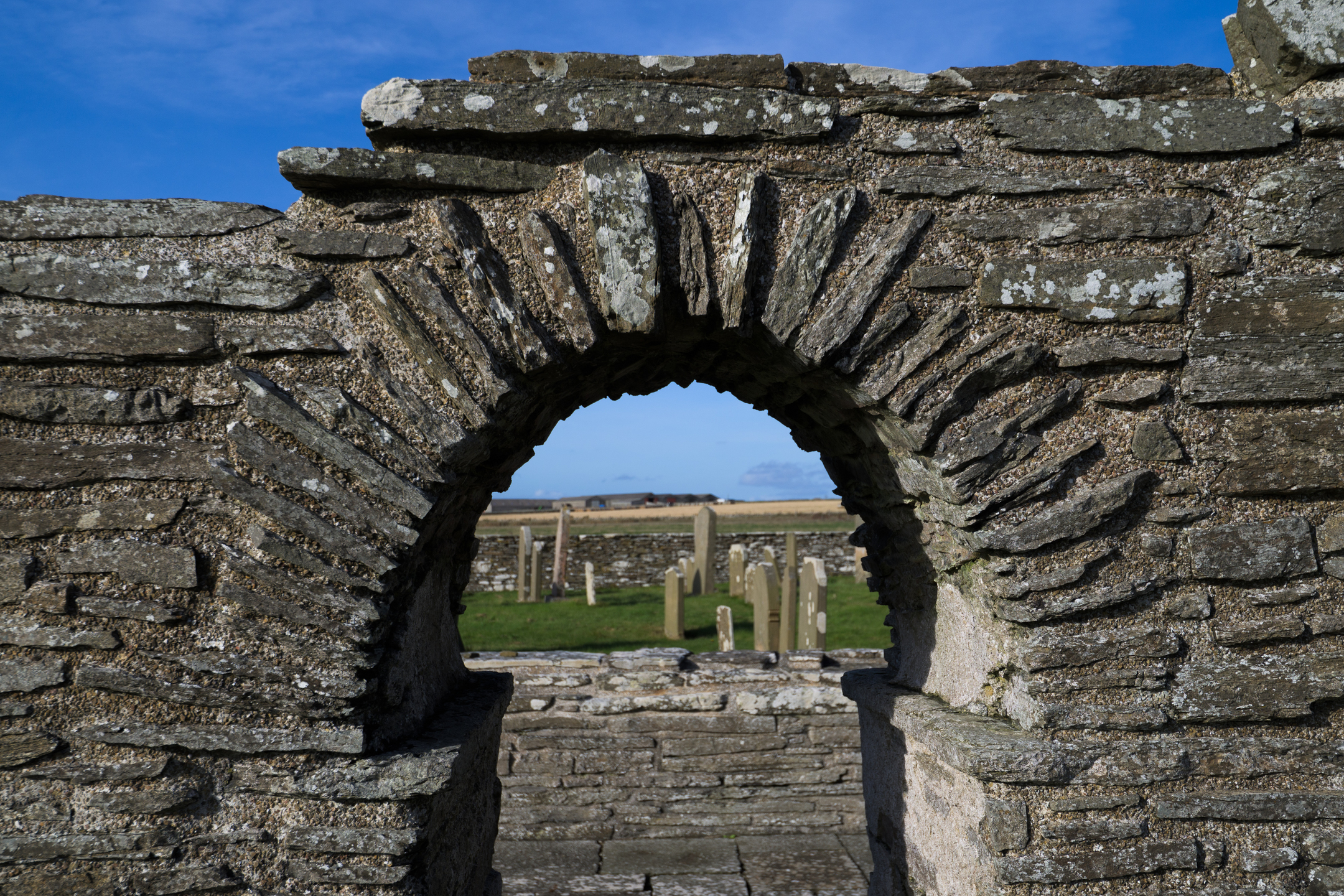 Close view of the stone arch in the wall of Westside Church, with gravestones and open farmland visible through the opening.