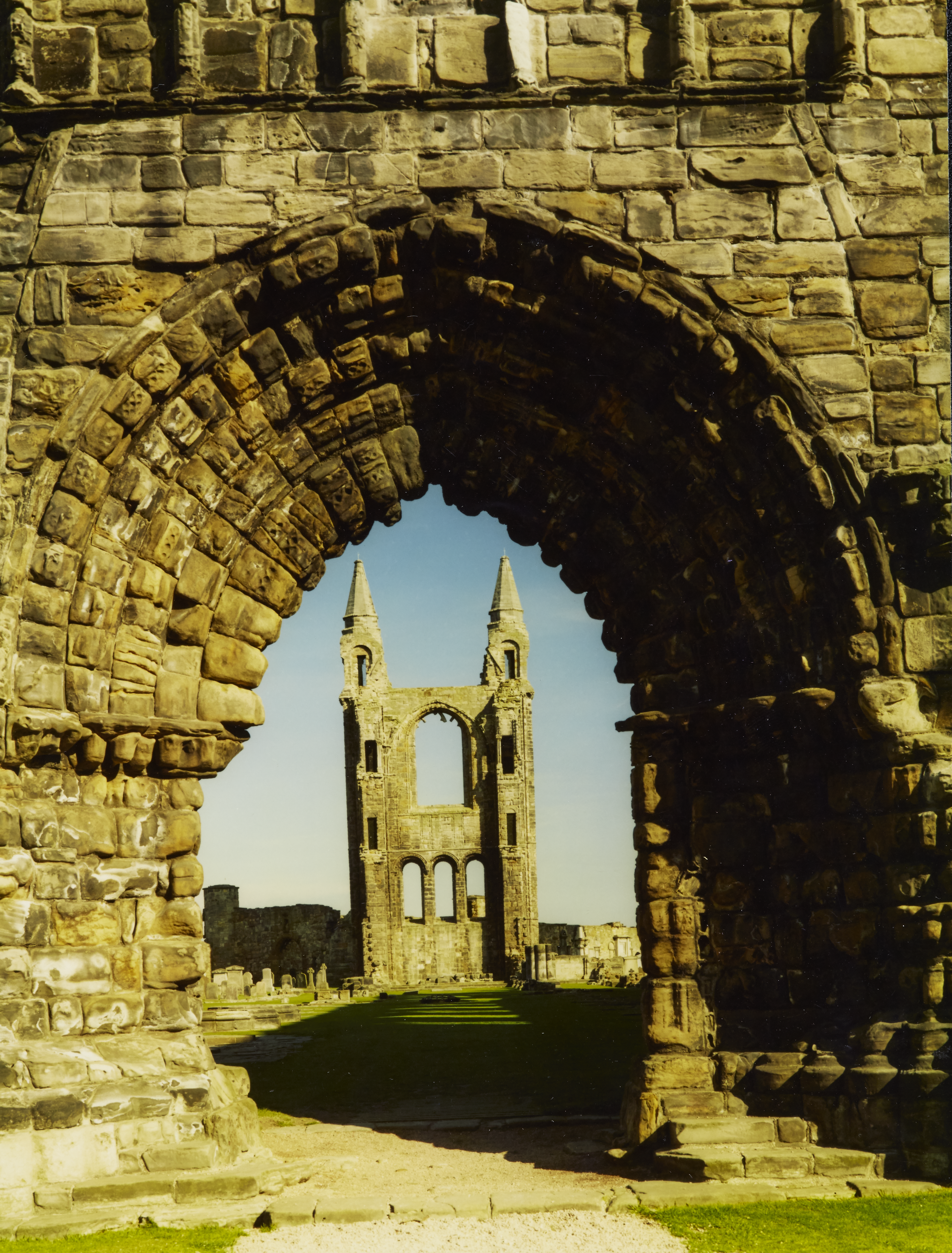 A tall portion of St Andrews Cathedral through an archway at the other end