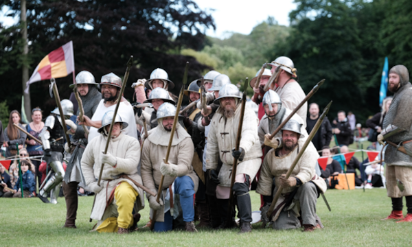 A group in costume on a battlefield raise their spears to the camera 