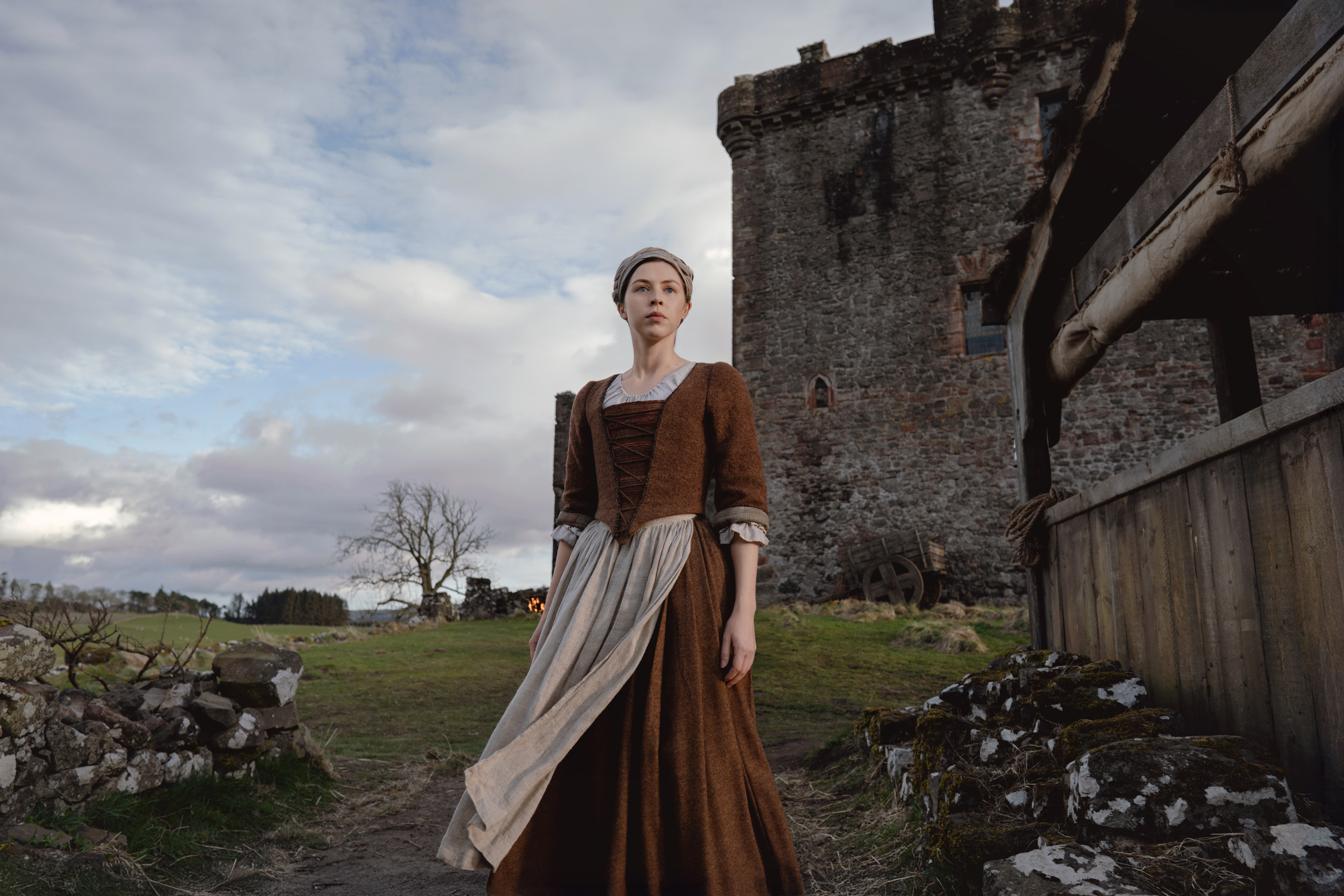 An actress in a historic dress pictured in front of a ruined castle.