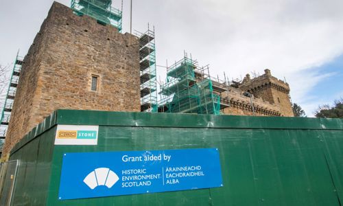A sign in front of a building reads ‘Grant aided by Historic Environment Scotland’. The building has scaffolding.