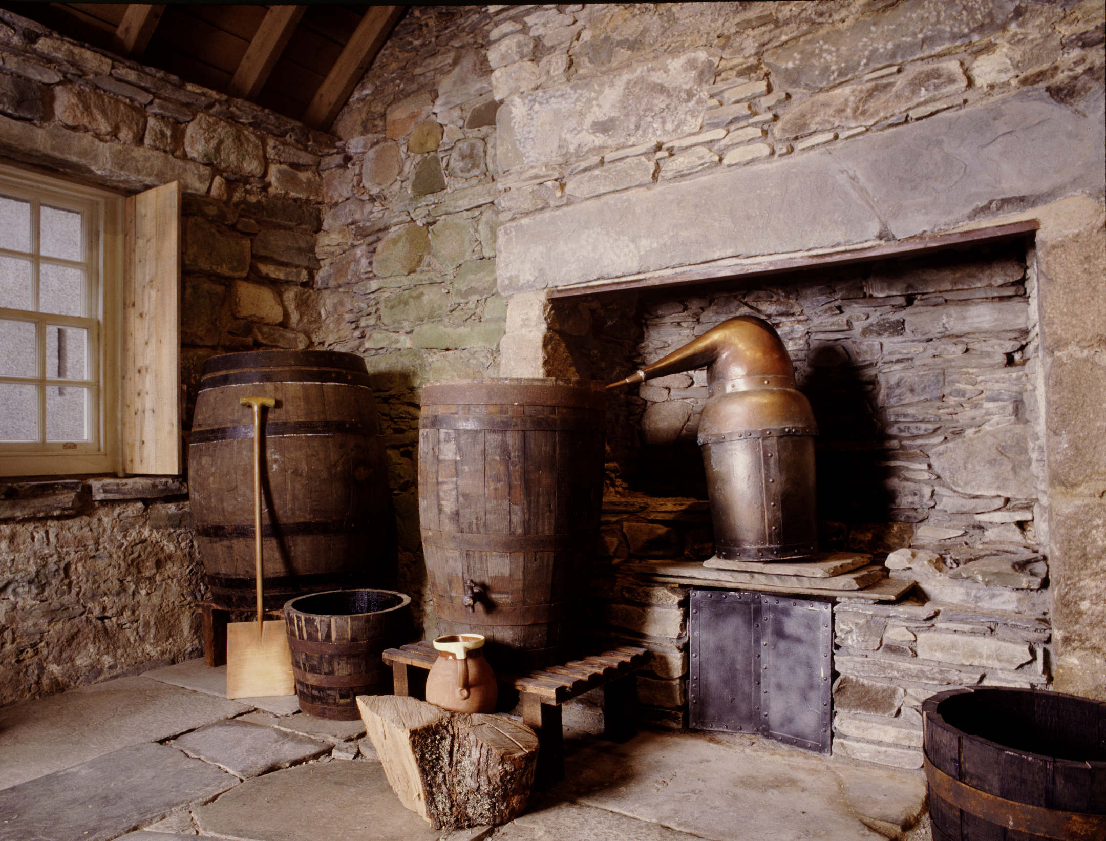 Interior scene showing wooden barrels, a copper still, and stone walls. A view of the castle’s historic distilling room.