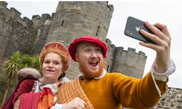 Two costumed performers smiling and taking a selfie with a castle behind them