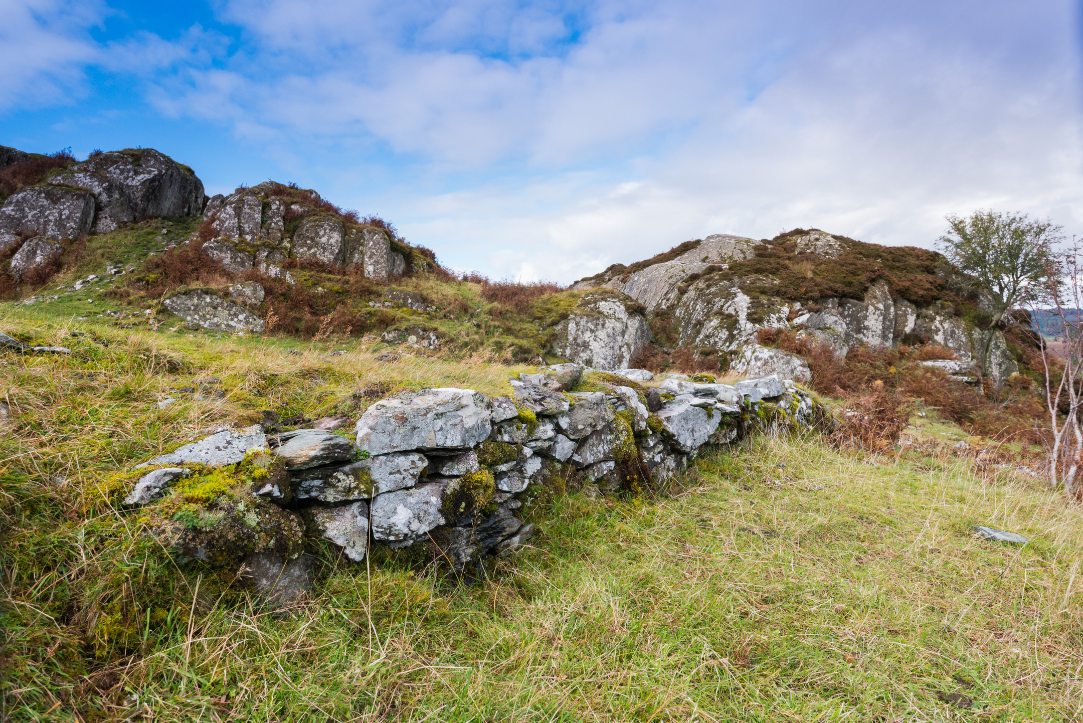 Moss-covered stone wall and rocky outcrops on the grassy slopes of Dunadd Hill.