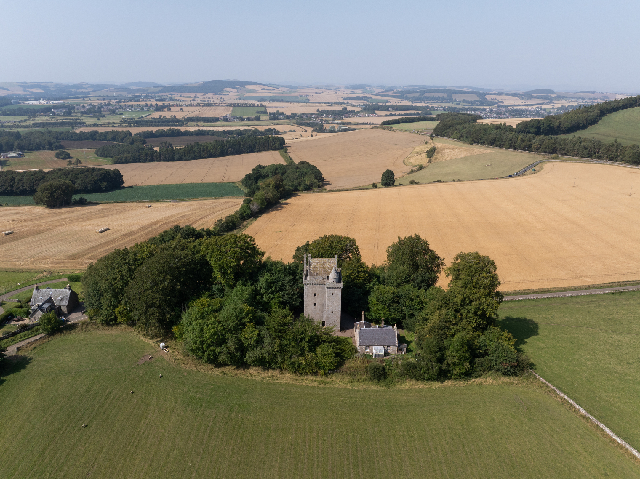 Aerial view of small tower surrounded by trees in among golden and green fields