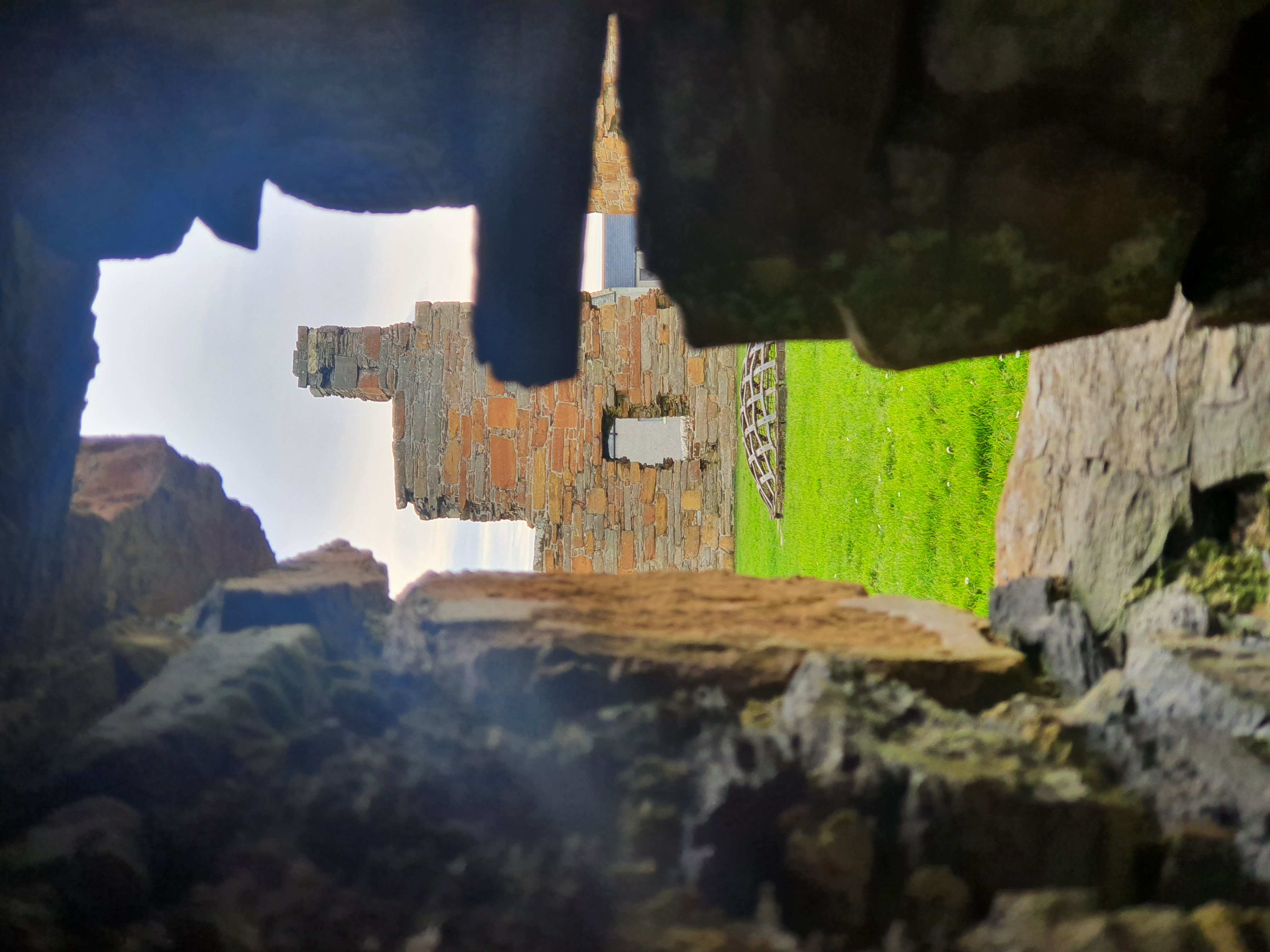 View through a narrow stone opening toward grassy courtyard and a ruined tower of Earl’s Palace.