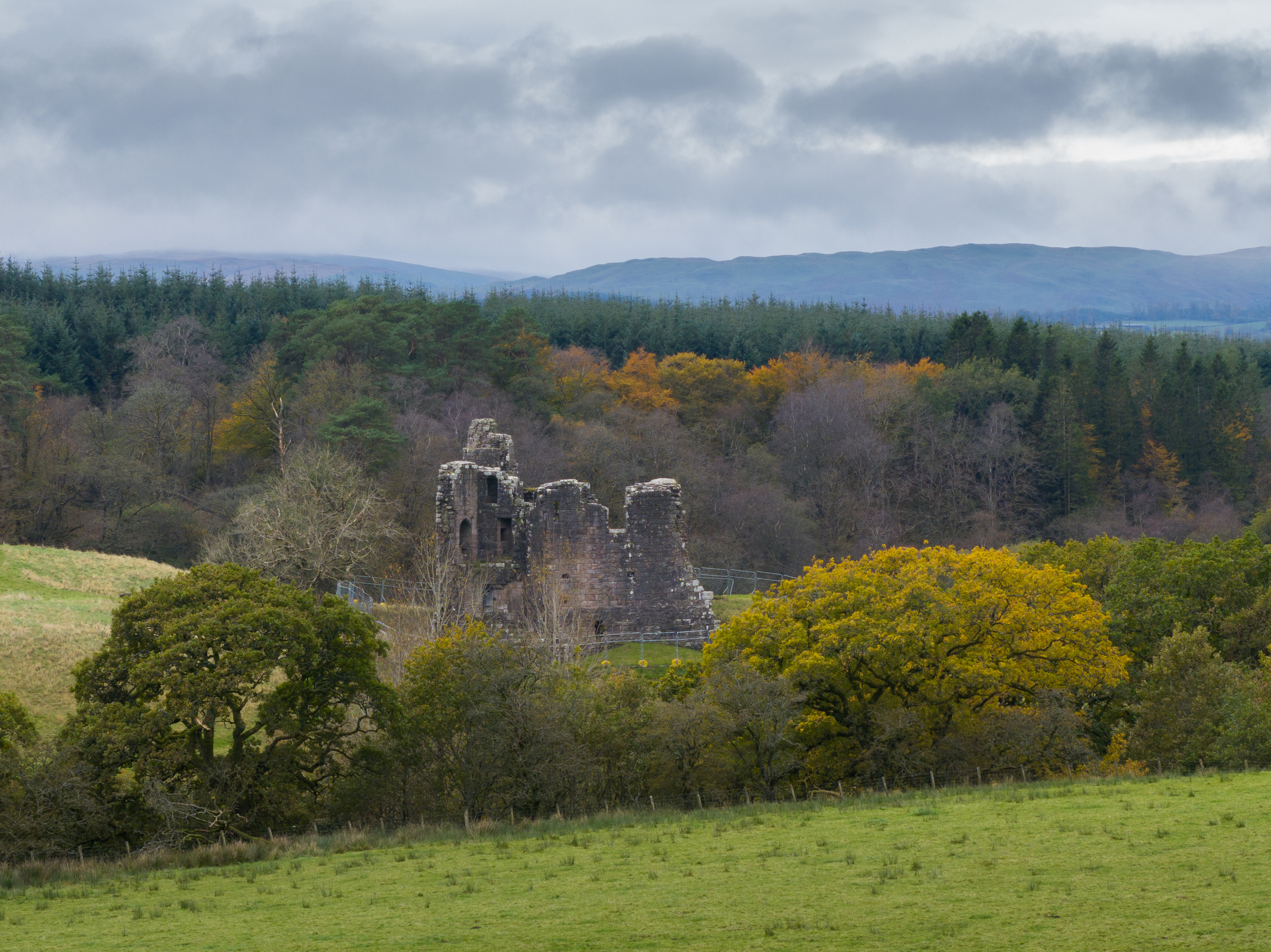 Aerial view looking level at Morton Castle with the autumnal woods in the background