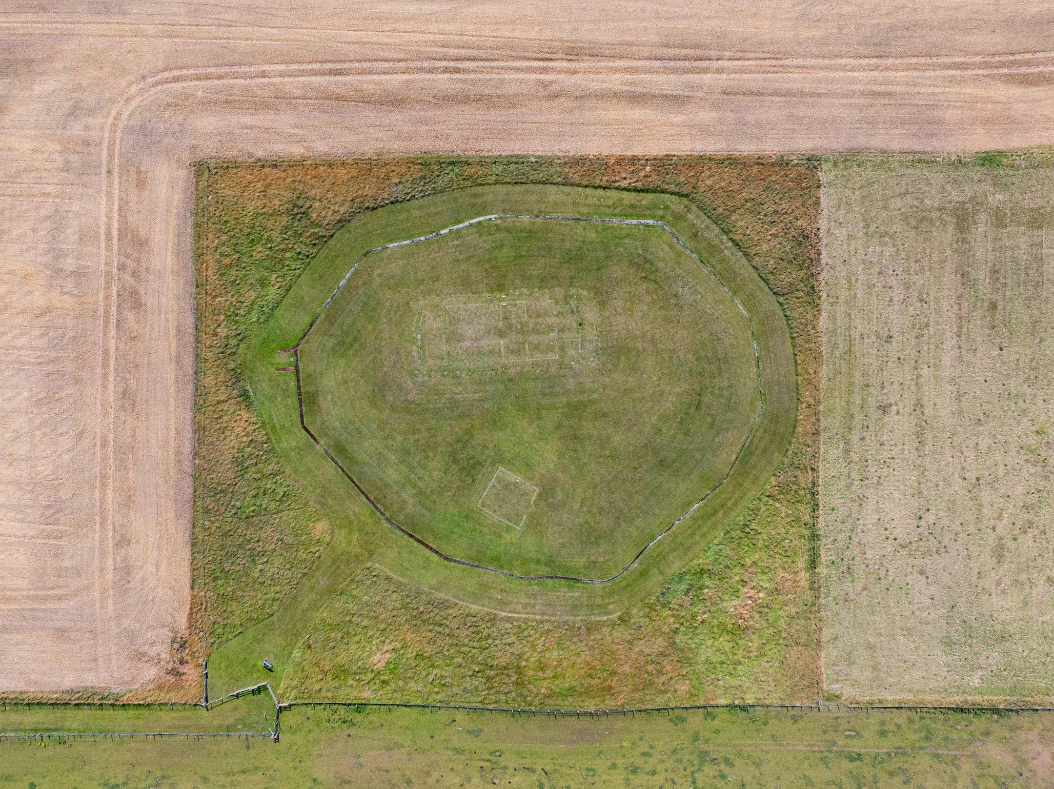 Aerial view of where a settlement once was, with distinctive round shape and outline of former building - surrounded by straight-edged fields