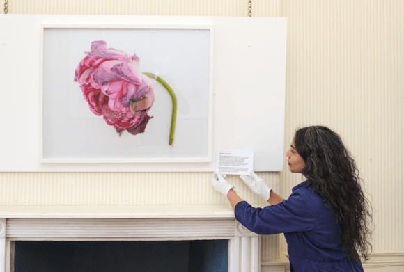 A woman adjusts an interpretation panel beside an artwork that depicts a wilting flower