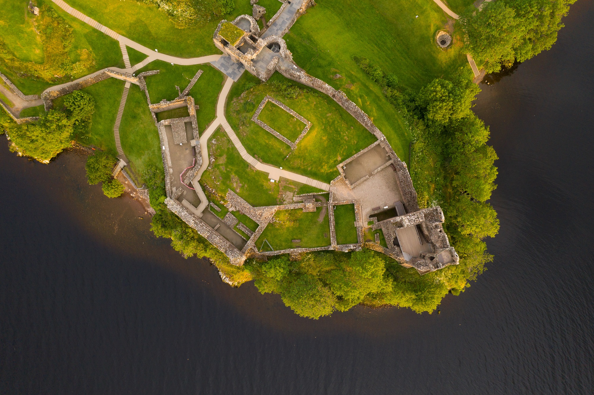 An aerial photo taken directly above the ruins of a castle. The bird's eye perspective shows the layout of the site, with paths criss-crossing between the remains of walls and buildings. 