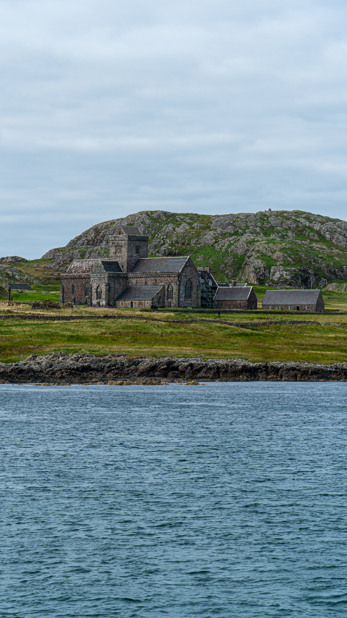 A large, historic stone abbey from the sea, with hills behind it