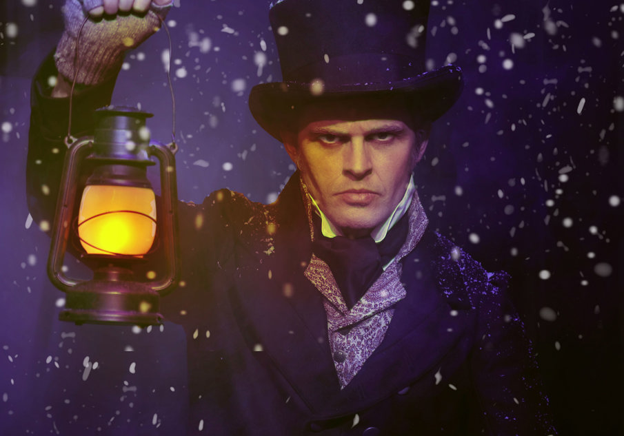 A man dressed as Ebeneezer Scrooge looking sternly at the camera holding up a lantern