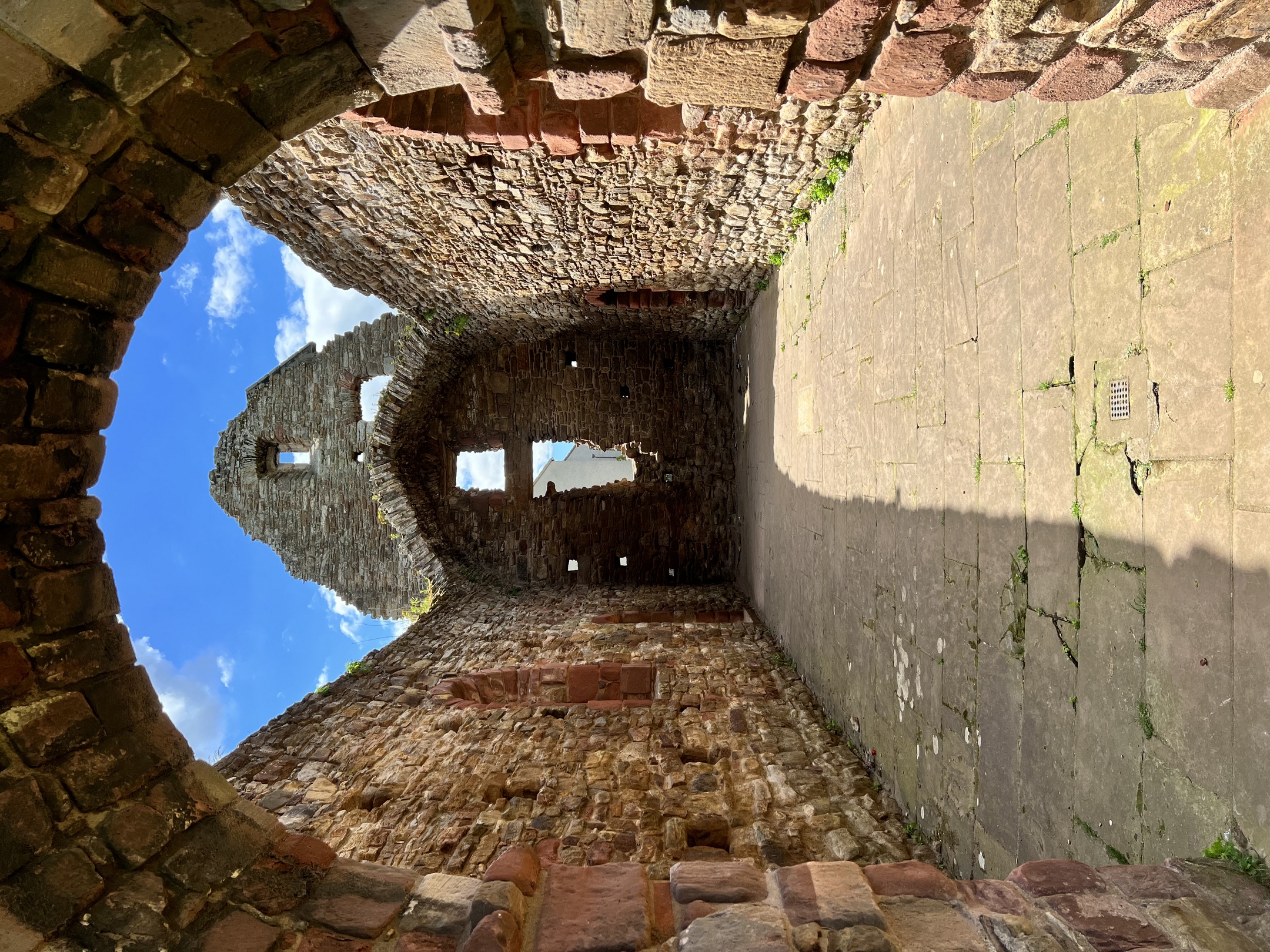 A view through a stone archway into the interior of a roofless ruined church. There is sunlight and shadow on the ancient stones.