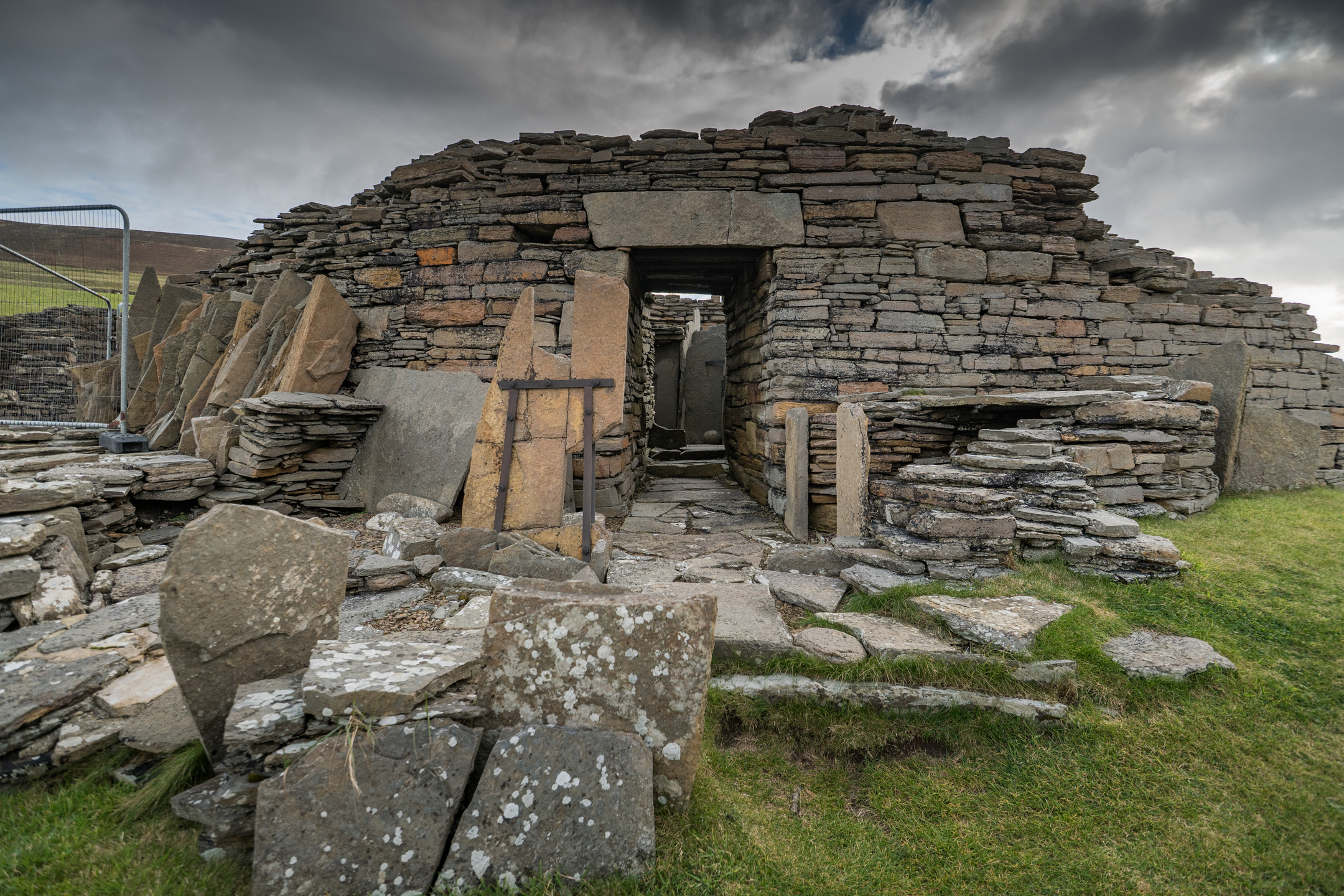The broch’s stone entrance framed by stacked slabs, leading into interior chambers filled with upright and fallen stones.