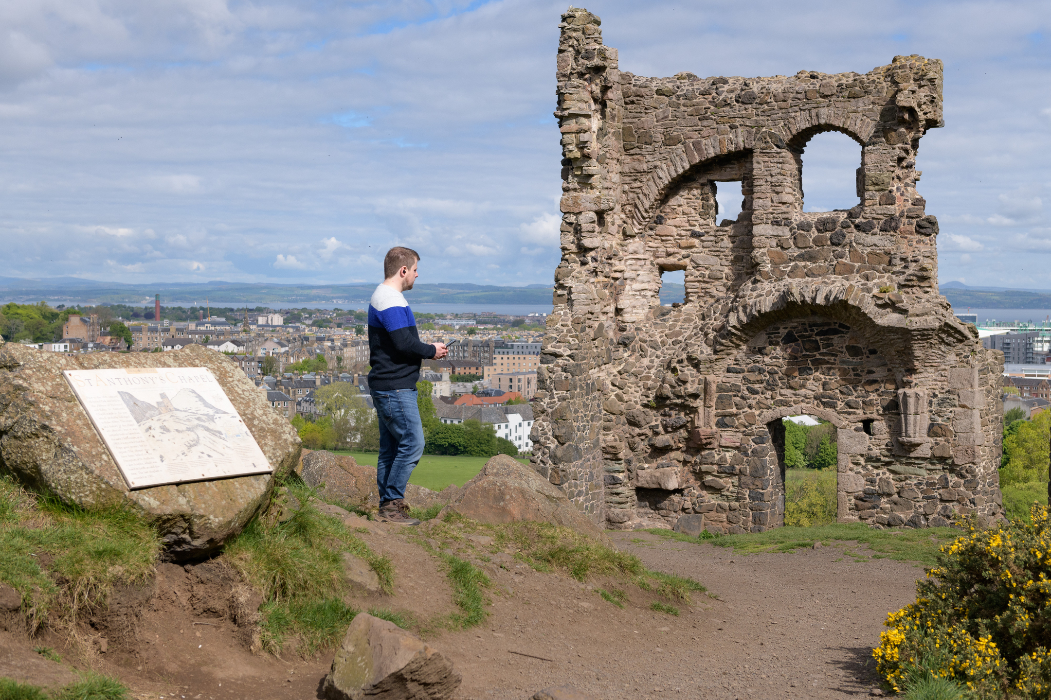 A man listens to audio content on his phone while admiring the ruins of a medieval chapel. 