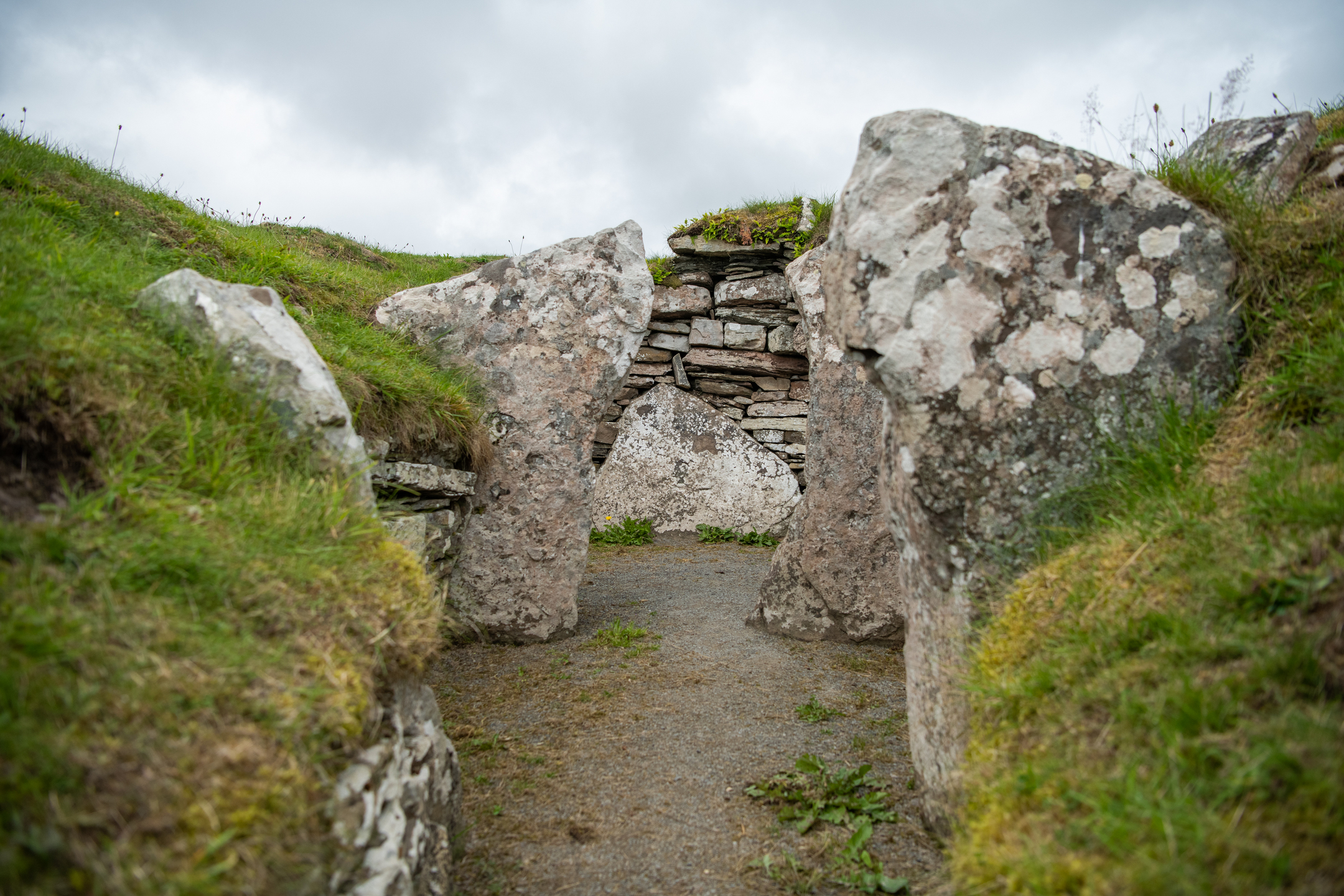 Inside a pathway between grassy mounds with stones cutting in, and a stone enclosure at the end