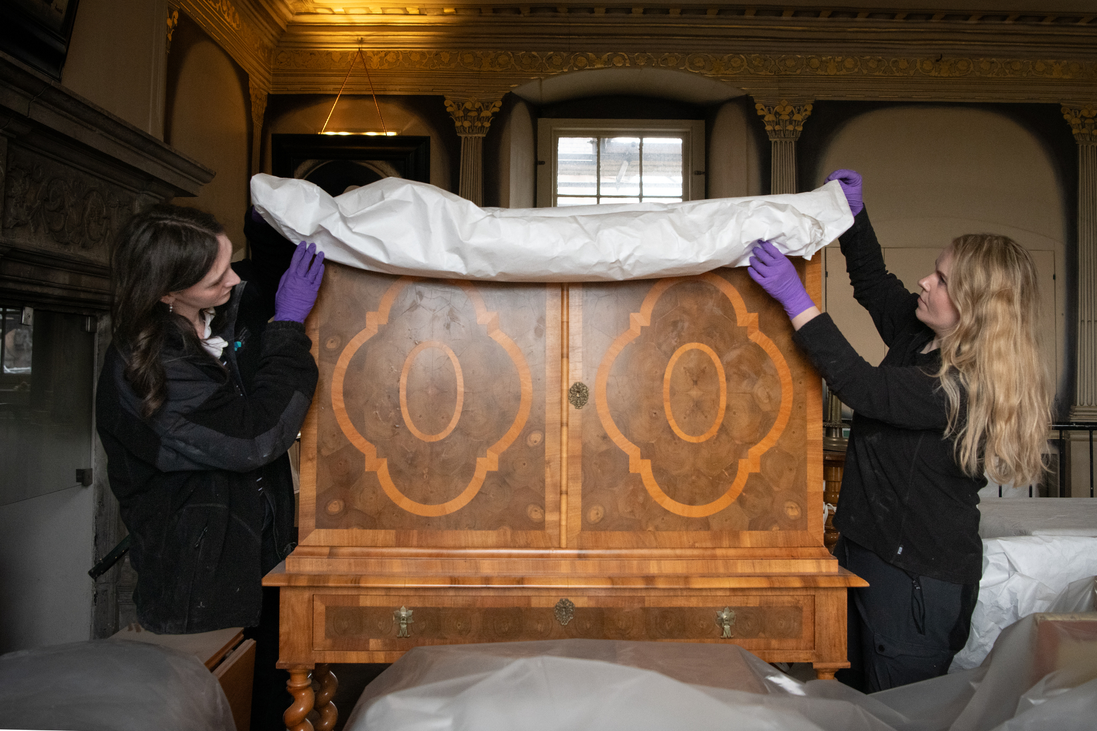 Members of the Historic Environment Scotland Collections team carefully remove a protective sheet from a historic dresser.