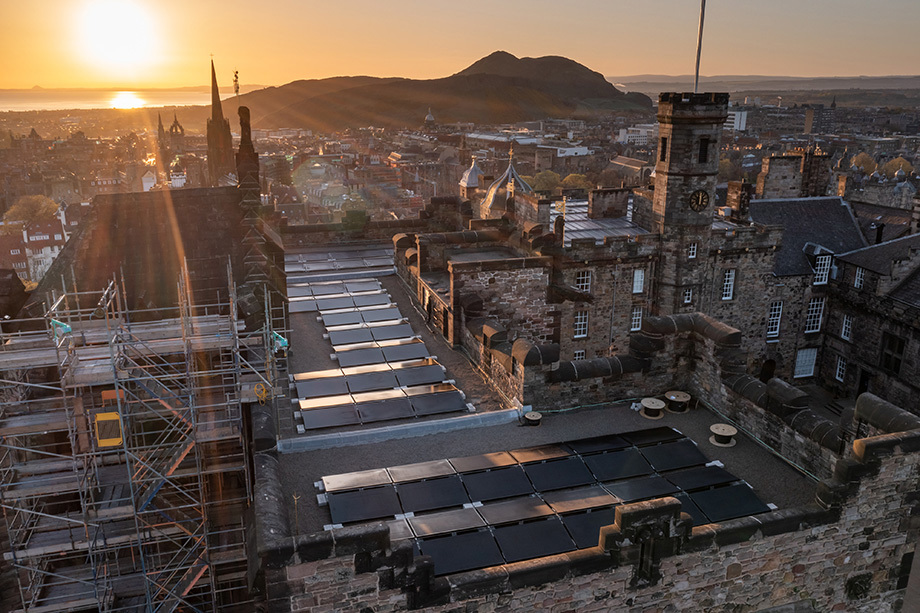 Solar panels on the rooftop of Edinburgh Castle. In the background the sun is rising over Arthur's Seat.