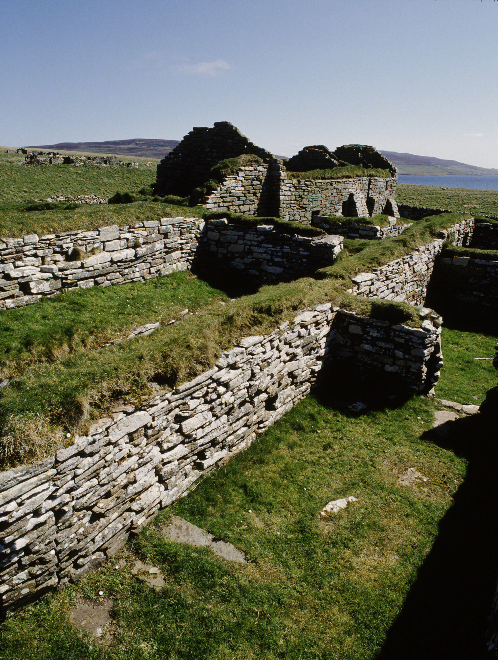 low stone walls with grass along the top and the roofless remains of an old croft building by the sea