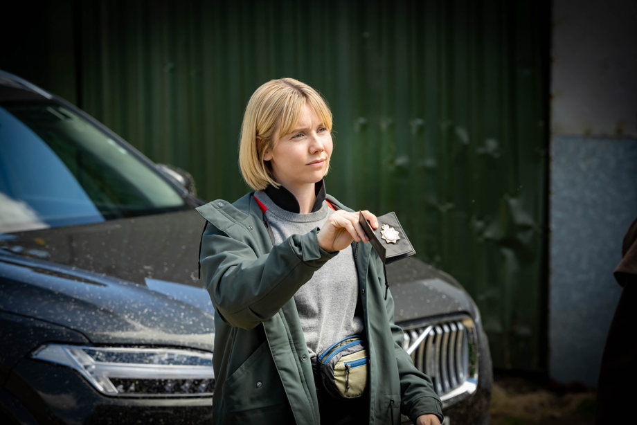 DS Karen Pirie standing in front of a car showing her police badge