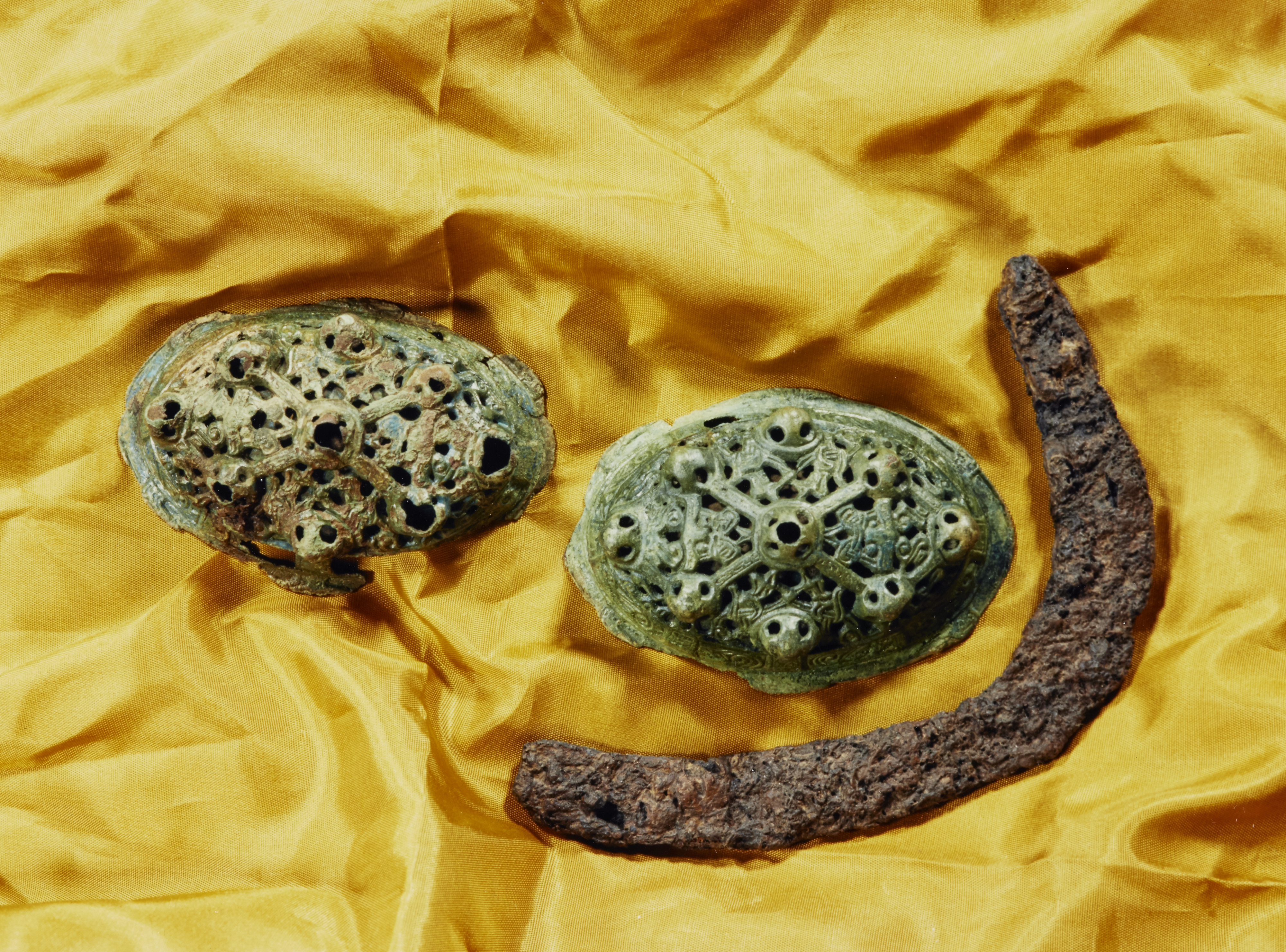 Three items on a piece of yellow fabric. Two are round, green items with patterns embossed and the third is brown and banana-shaped