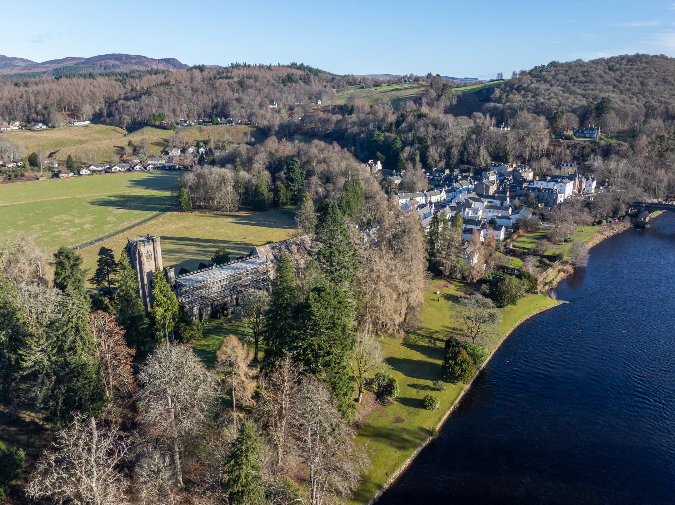 An aerial view of a historic cathedral attractively positioned next to large river, with countryside and a small town in the background.