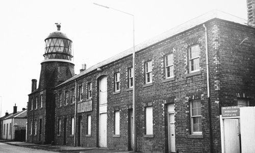 A lighthouse and large brick building presented in black and white