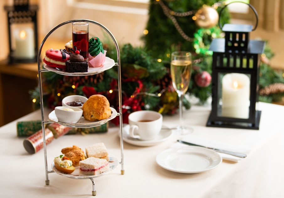 Afternoon tea laid out with a cake stand adorning lovely treats, cups and saucers, a lantern and christmas decorations